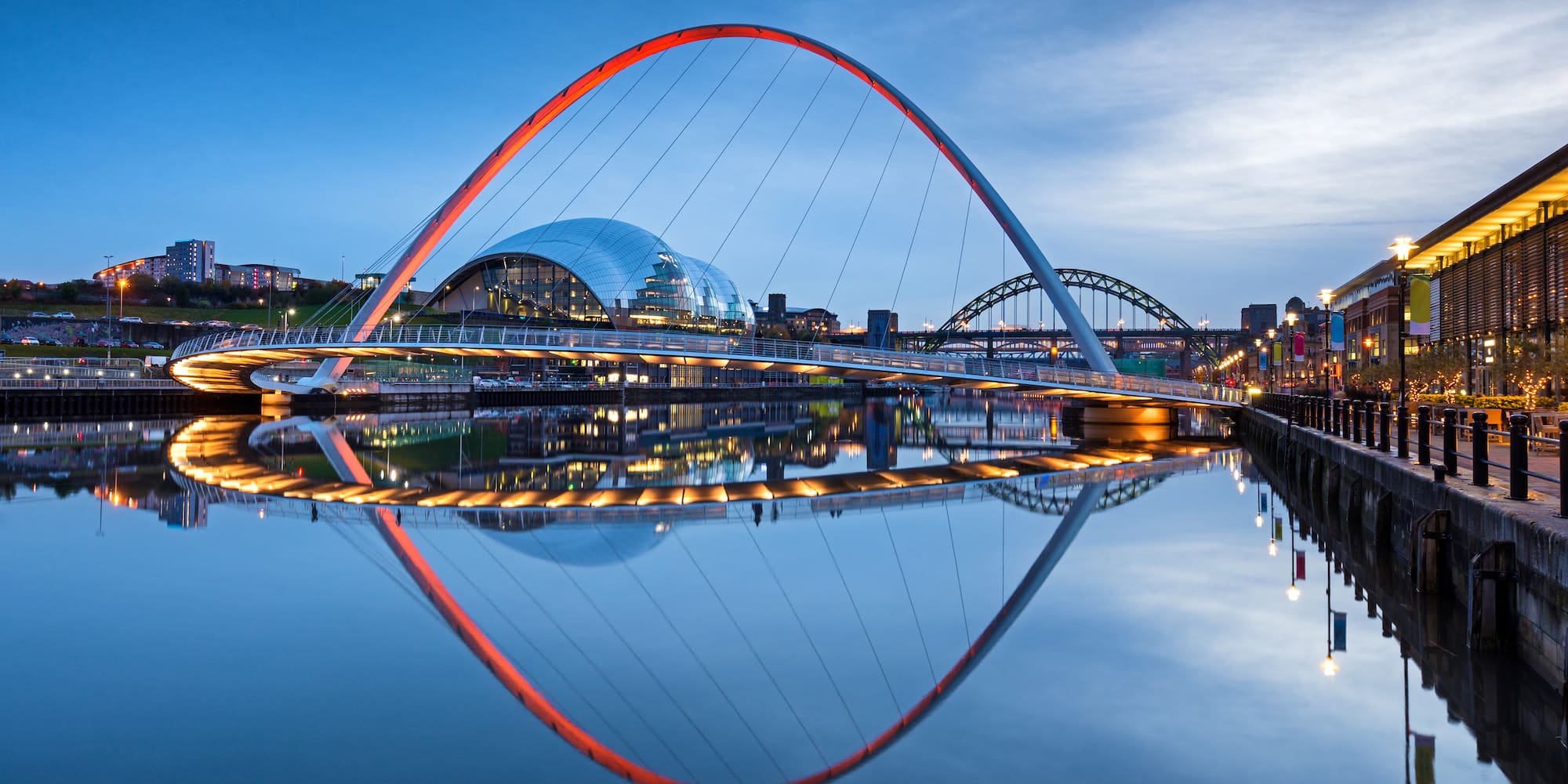 Gateshead Millennium Bridge illuminated red at dusk, reflecting on River Tyne.