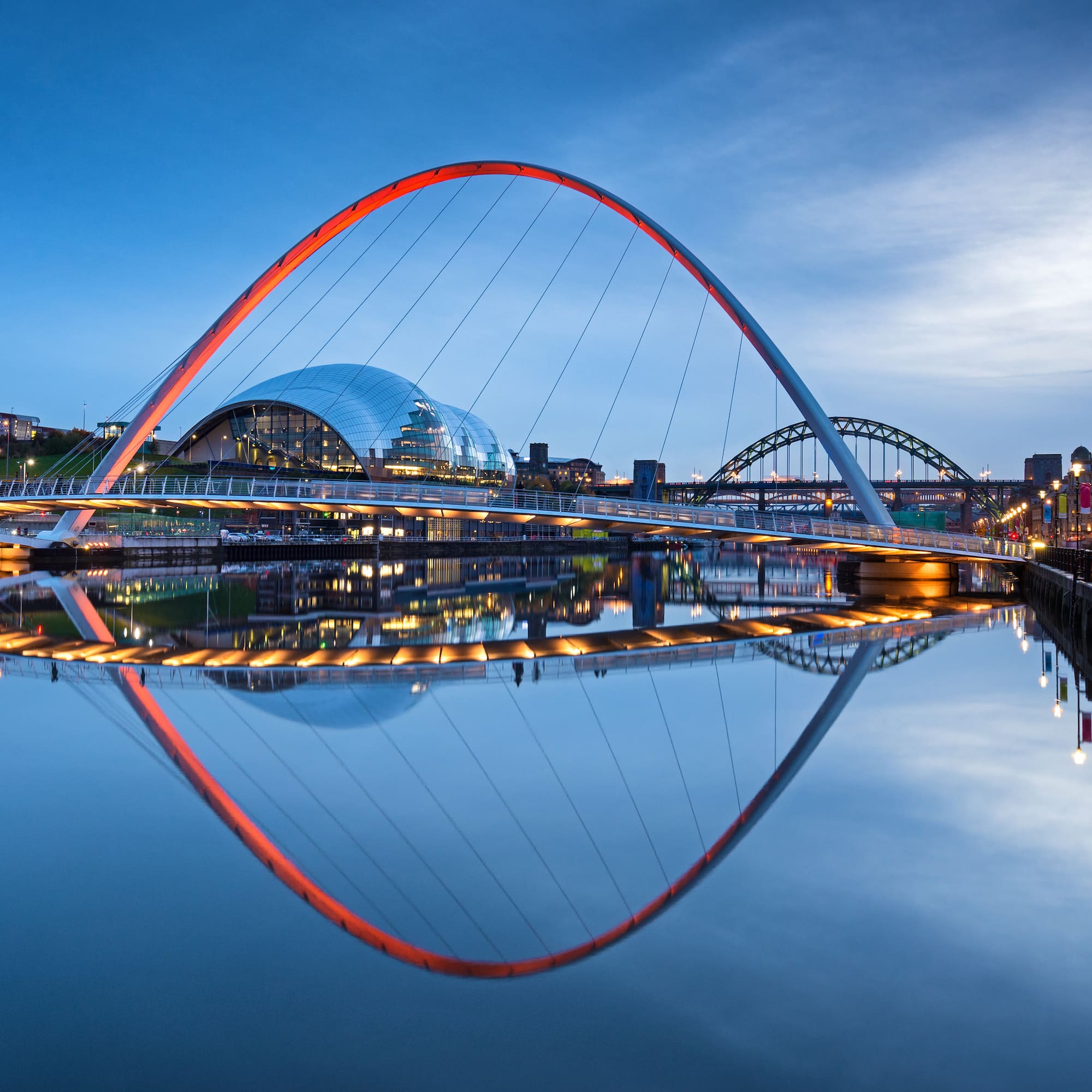 Gateshead Millennium Bridge illuminated red at dusk, reflecting on River Tyne.