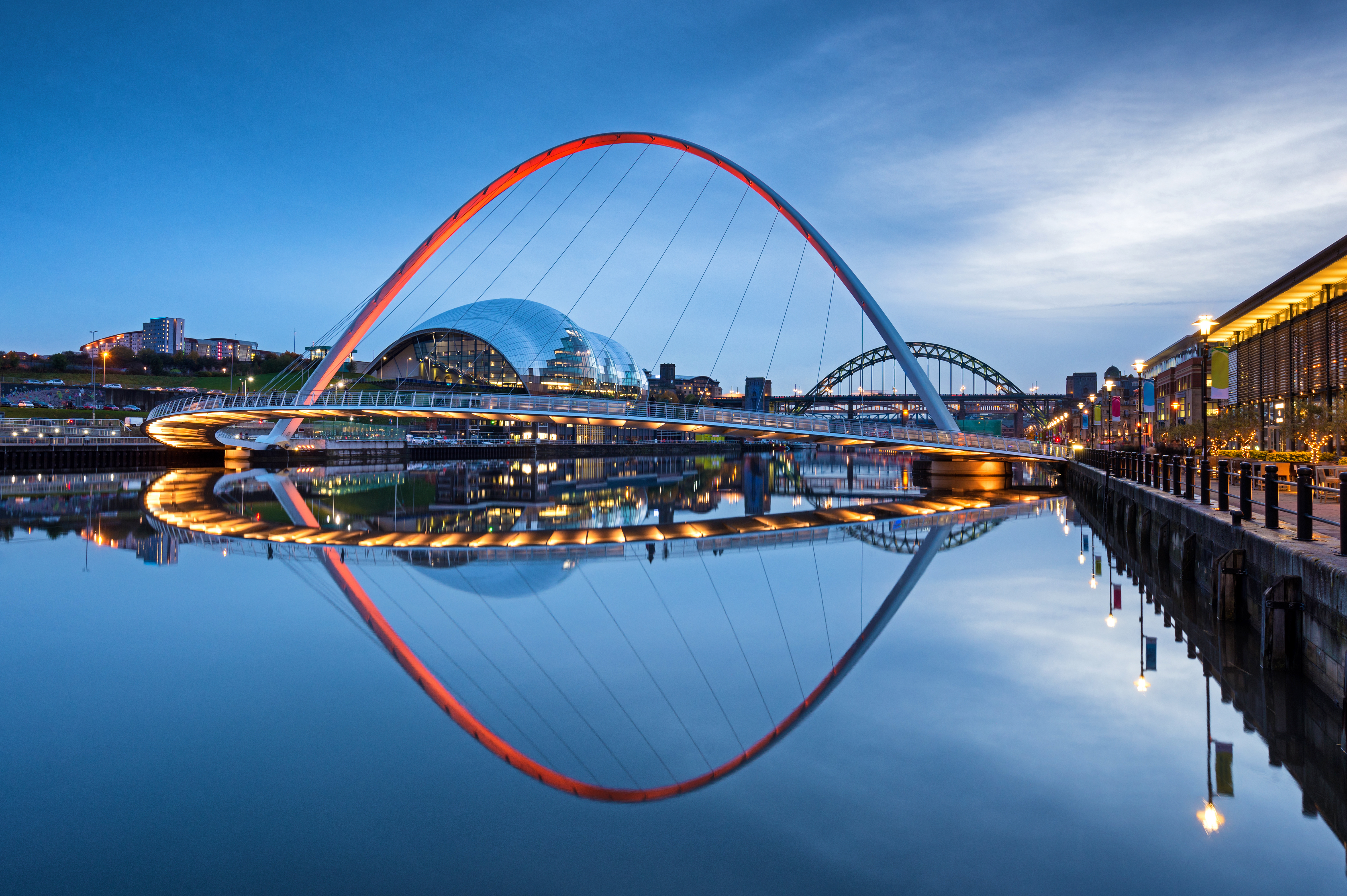 Gateshead Millennium Bridge illuminated red at dusk, reflecting on River Tyne.