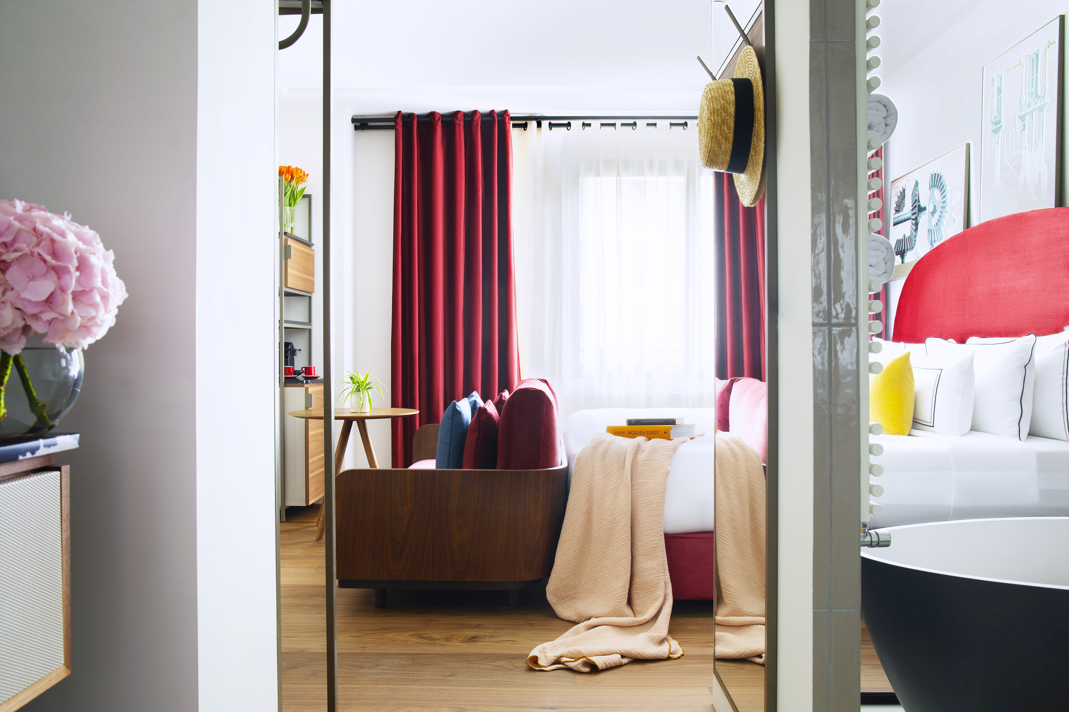 Vibrant hotel room with red curtains, bed, modern wooden furniture, and tub.