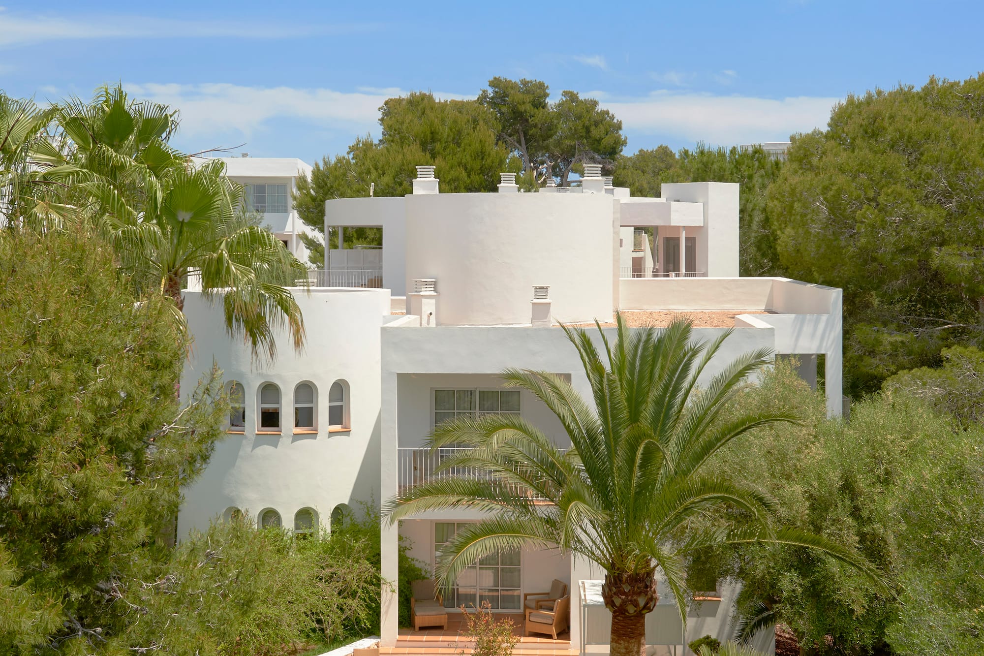 White Mediterranean villa with palm trees, sunny lawn, patio, and loungers.