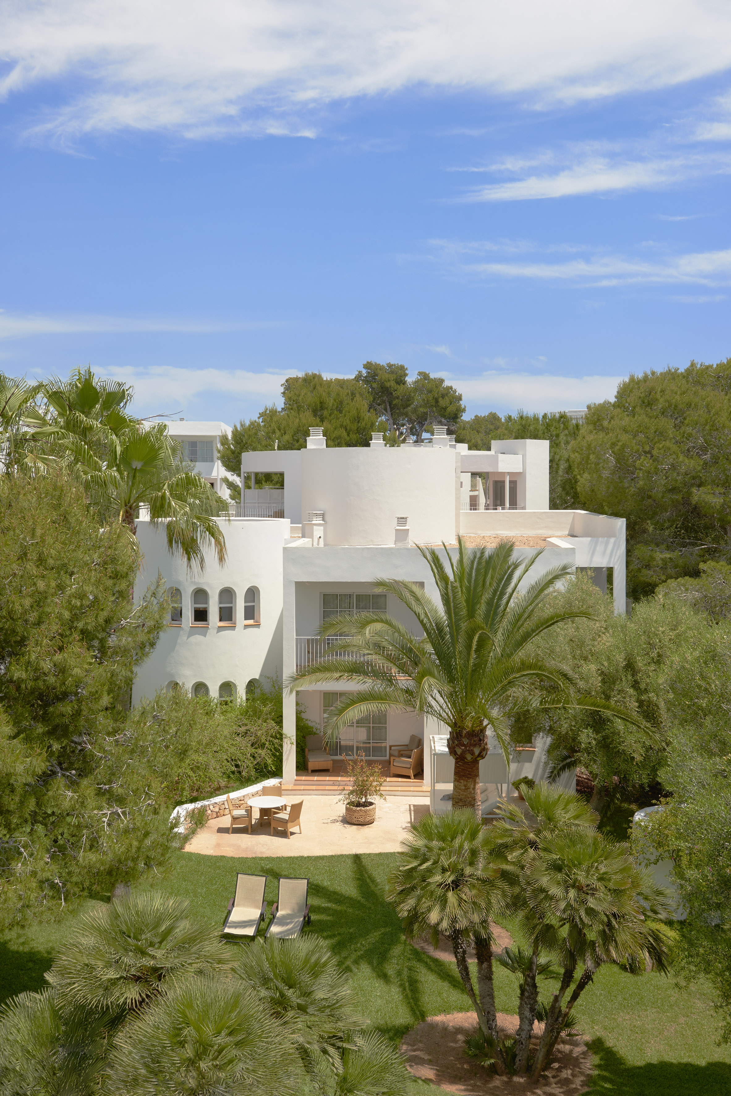 White Mediterranean villa with palm trees, sunny lawn, patio, and loungers.