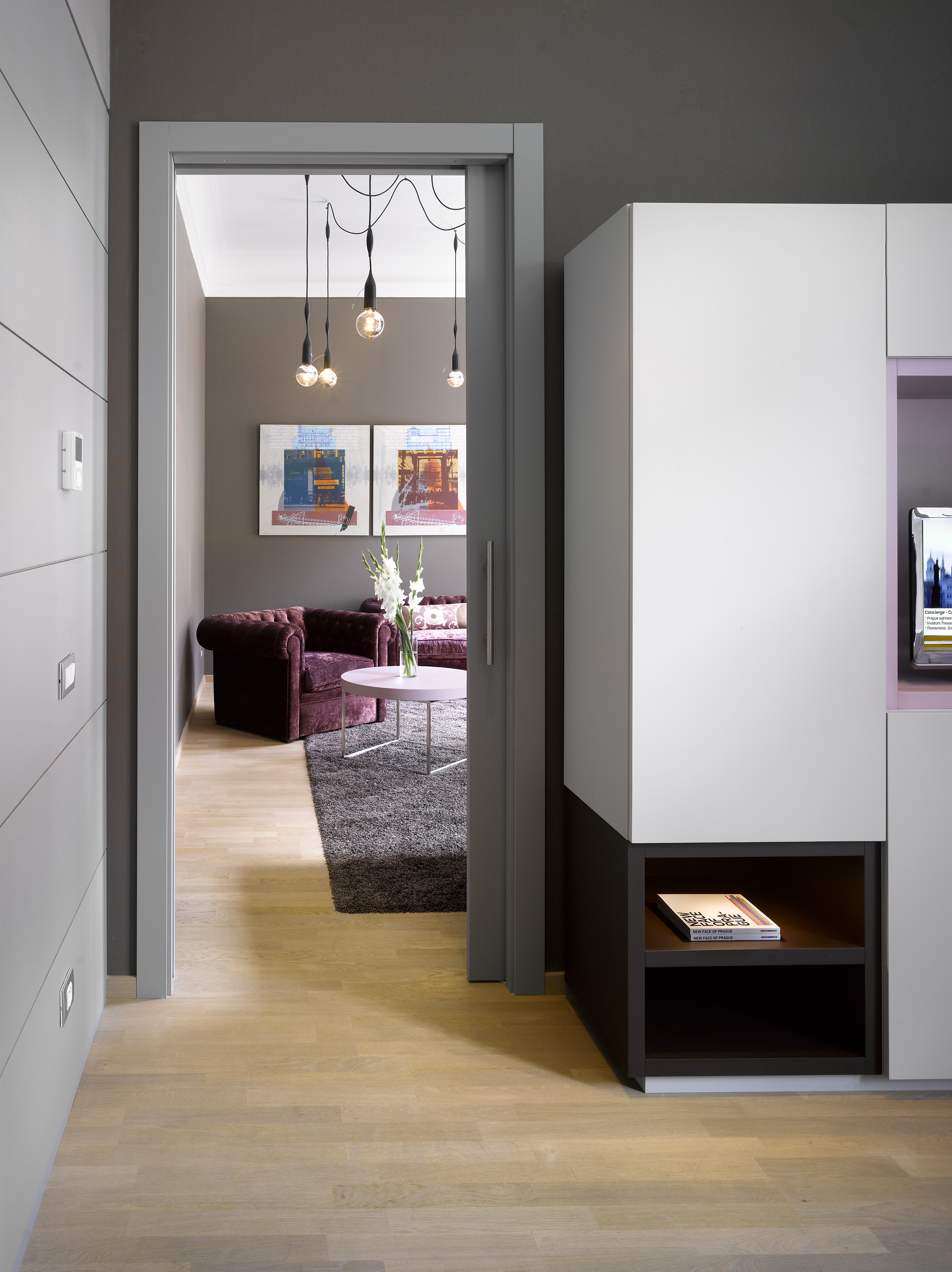 Modern living room with purple velvet sofa, art, wood floor, and pendant lights.