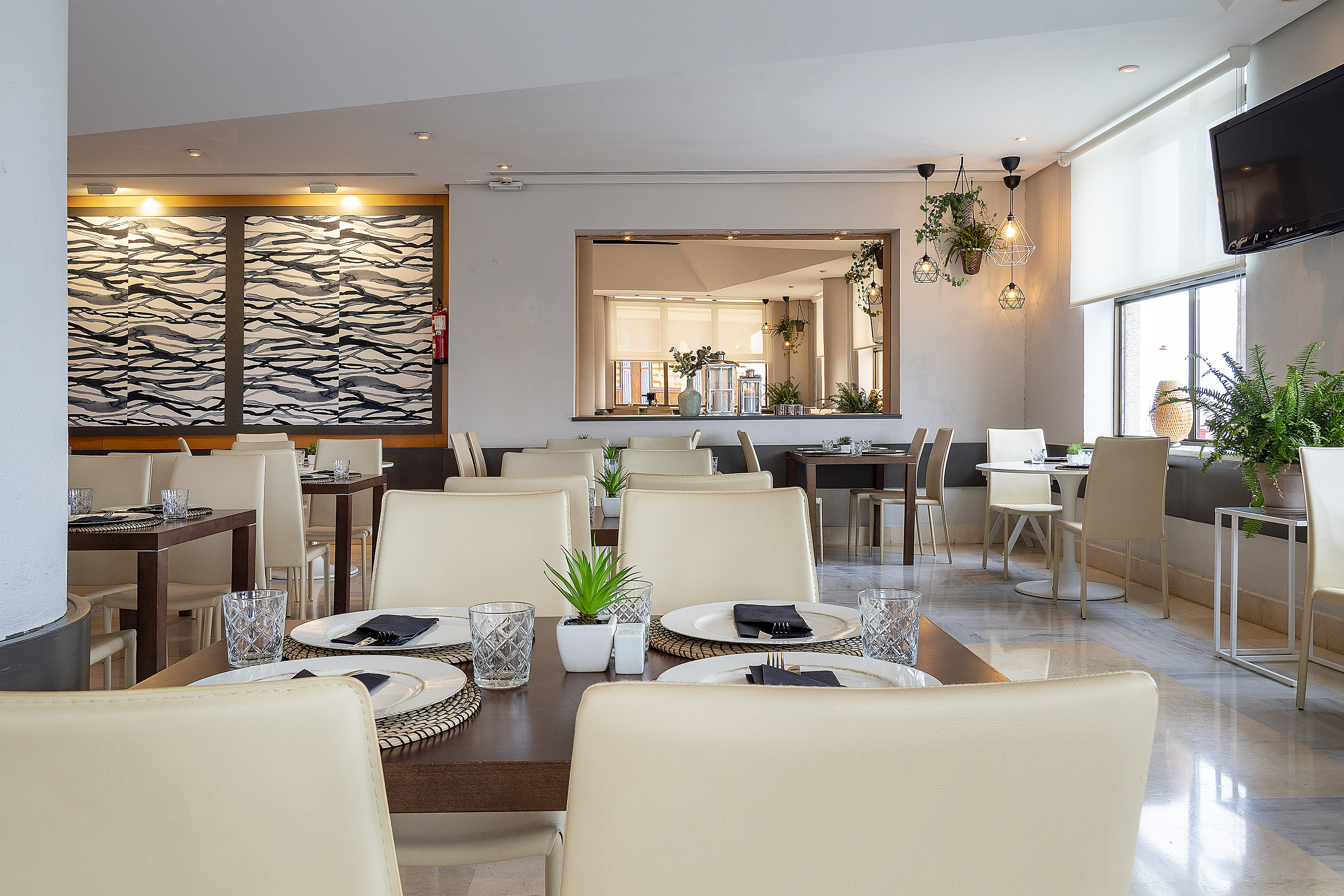 Modern hotel dining room with beige chairs, set tables, and stylish decor.