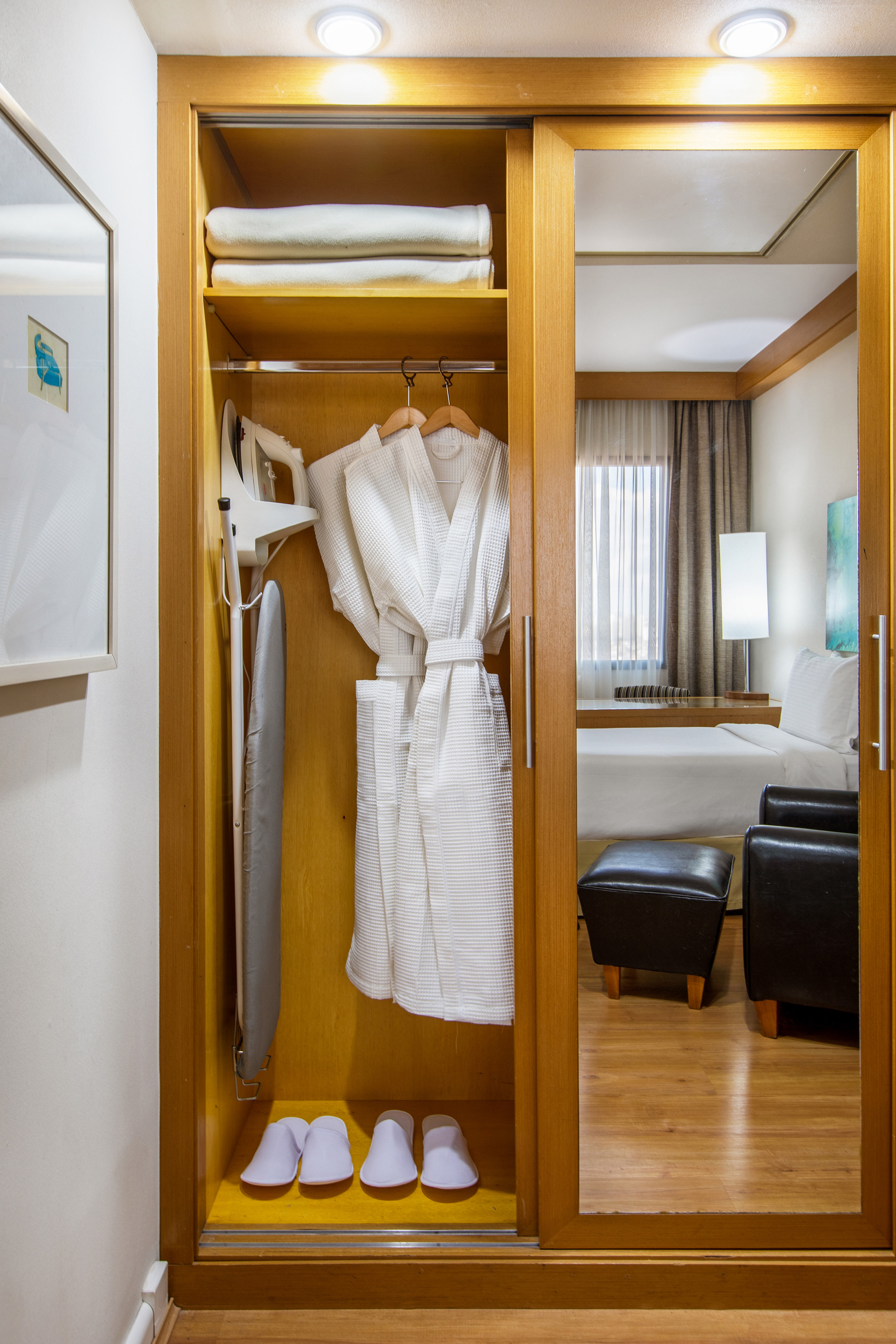 Hotel closet with bathrobes, iron, slippers, towels. Reflects bedroom interior.