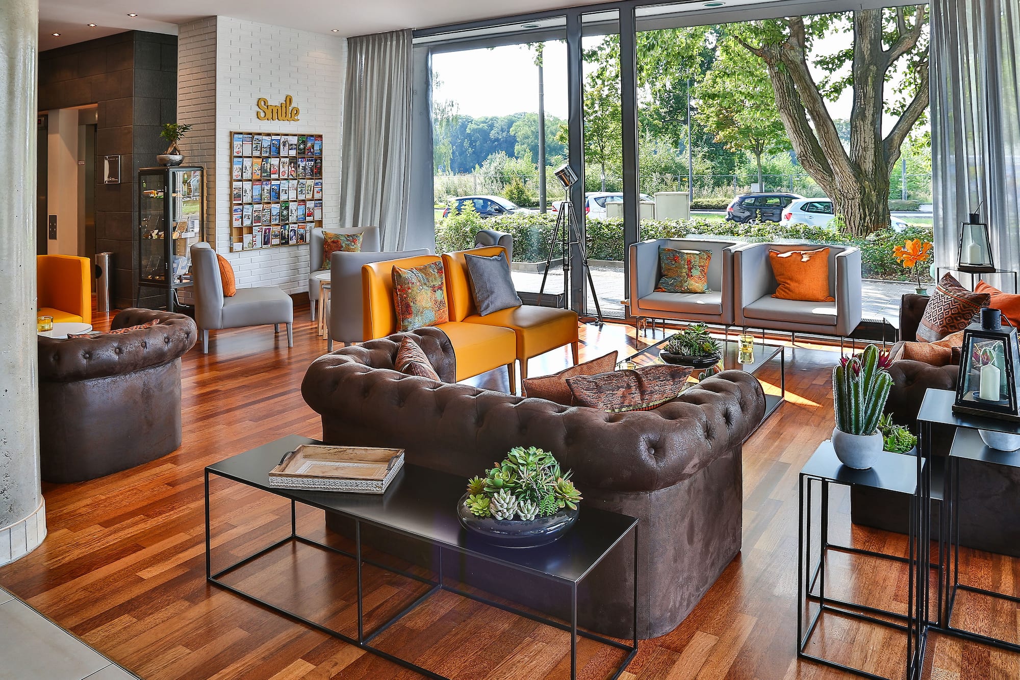 Modern hotel lobby with brown and orange seating, wood floor, and large windows.