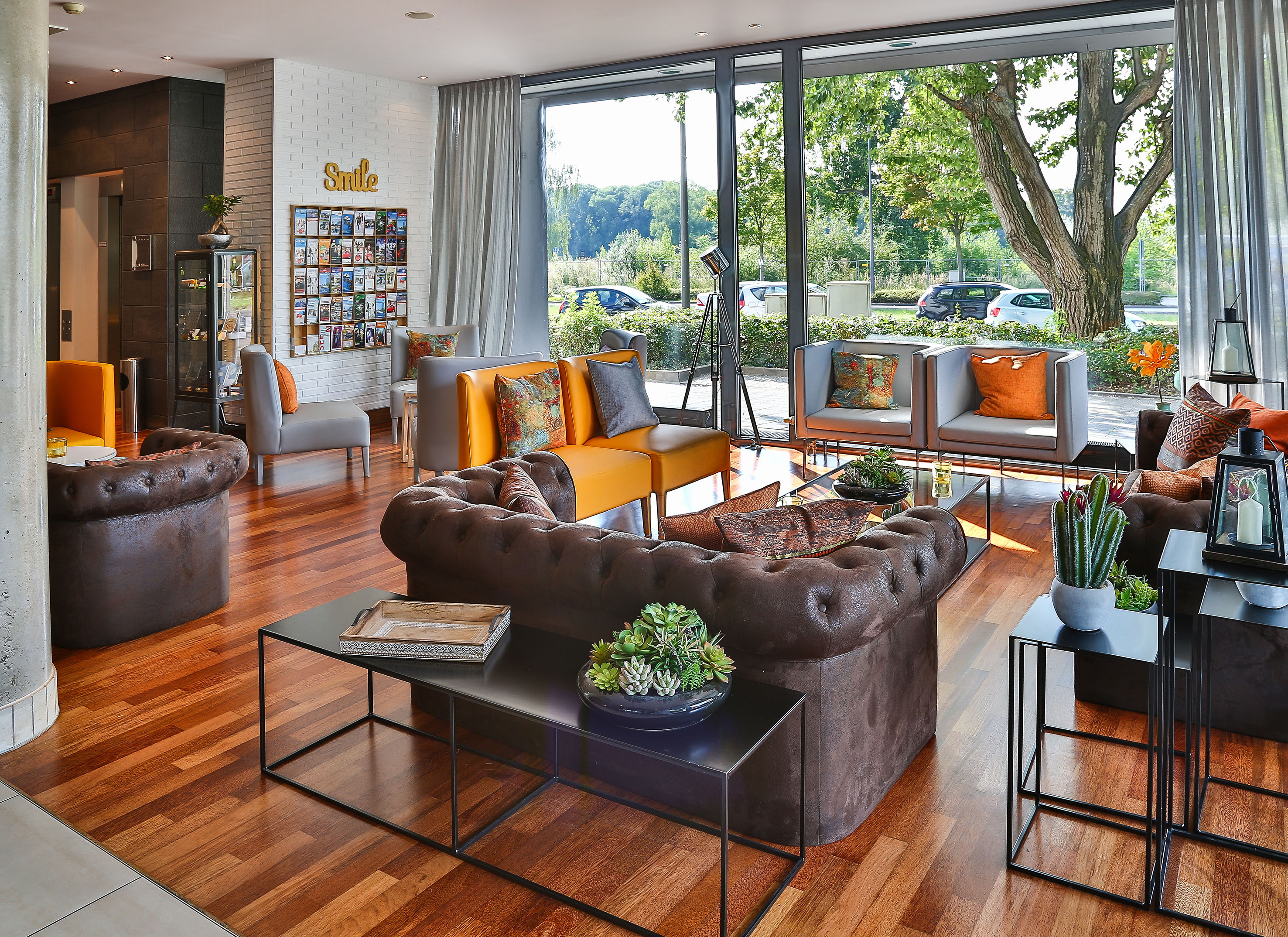 Modern hotel lobby with brown and orange seating, wood floor, and large windows.