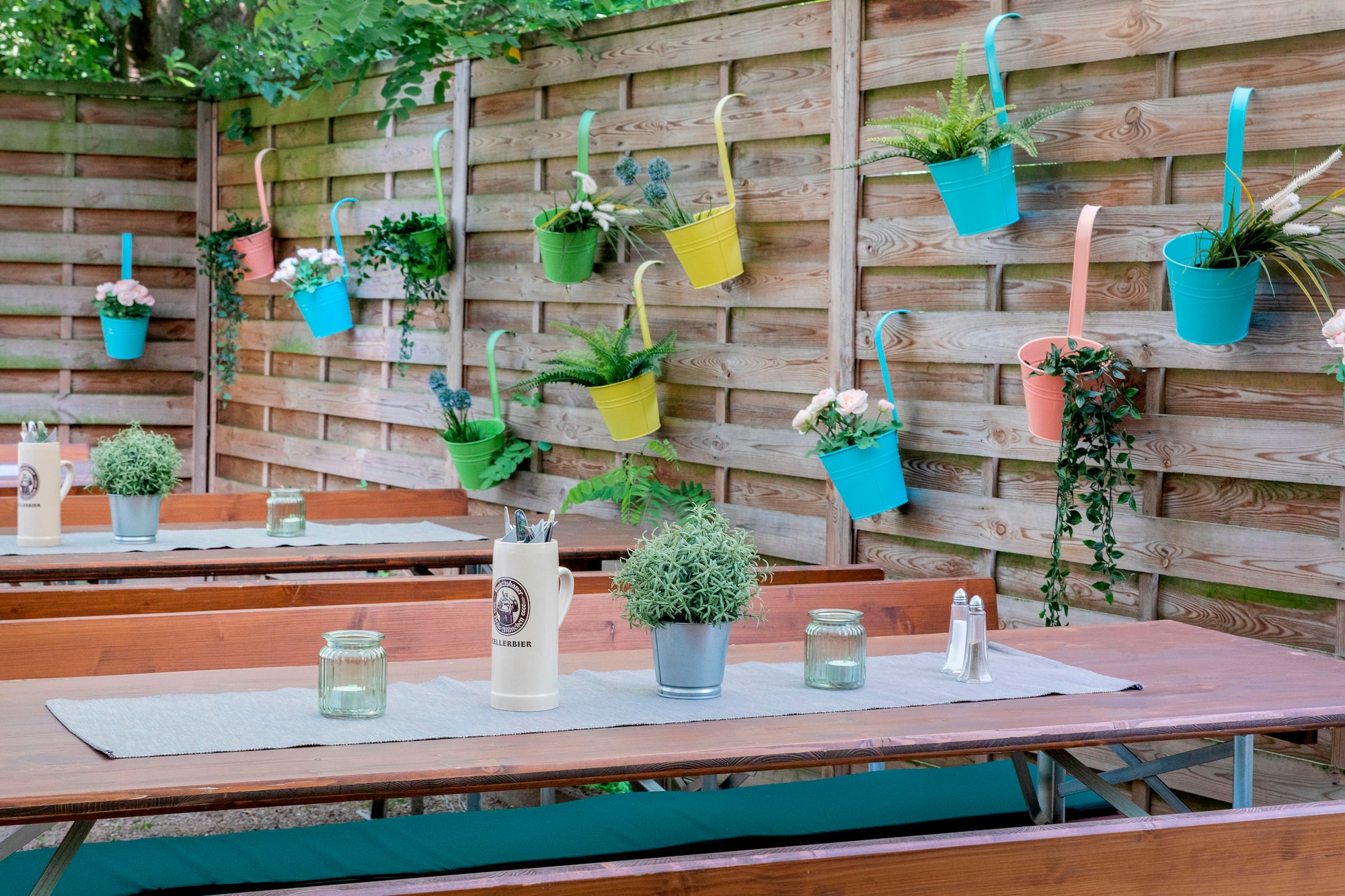 Colorful planters hanging on a wooden fence above outdoor picnic tables.