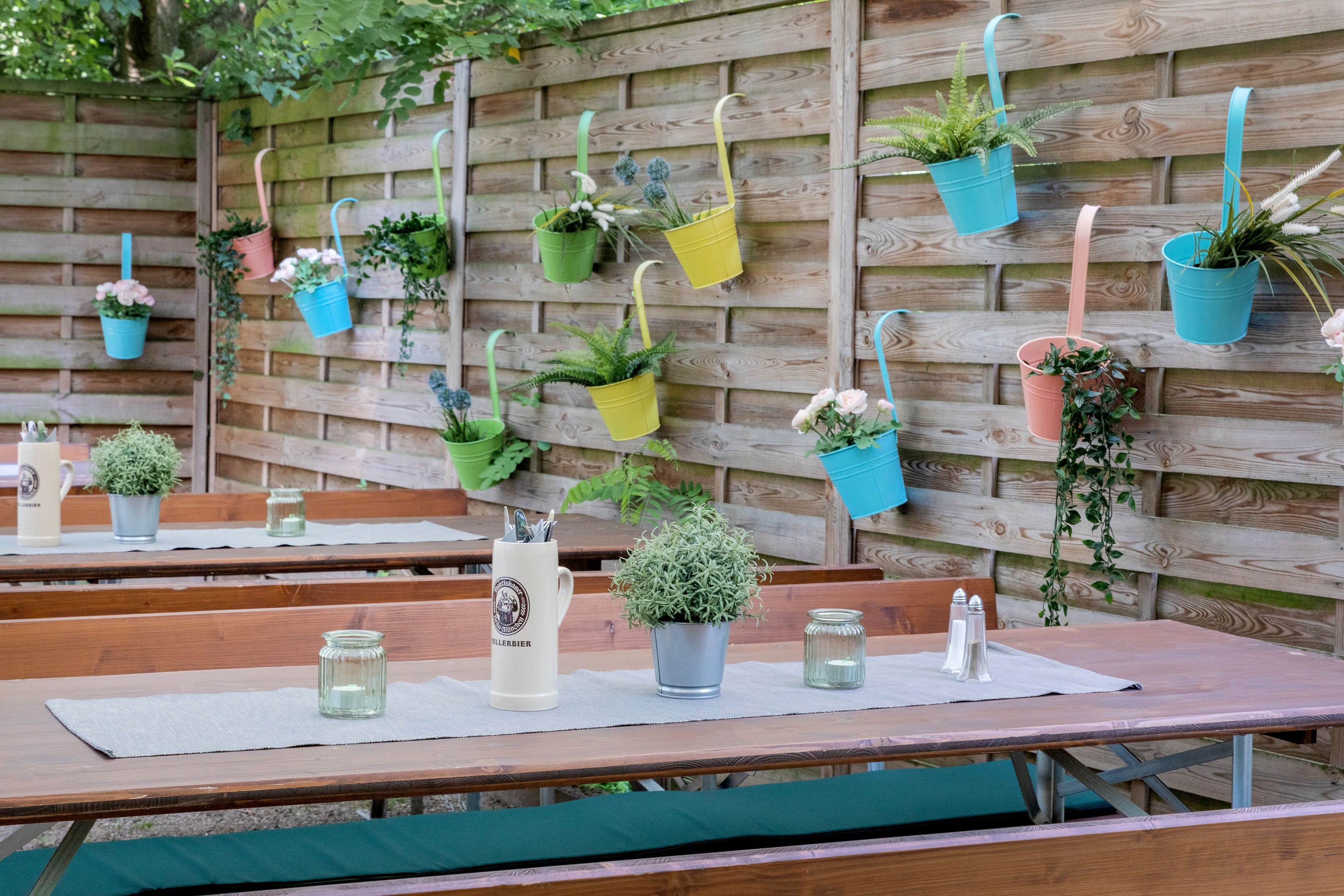 Colorful planters hanging on a wooden fence above outdoor picnic tables.