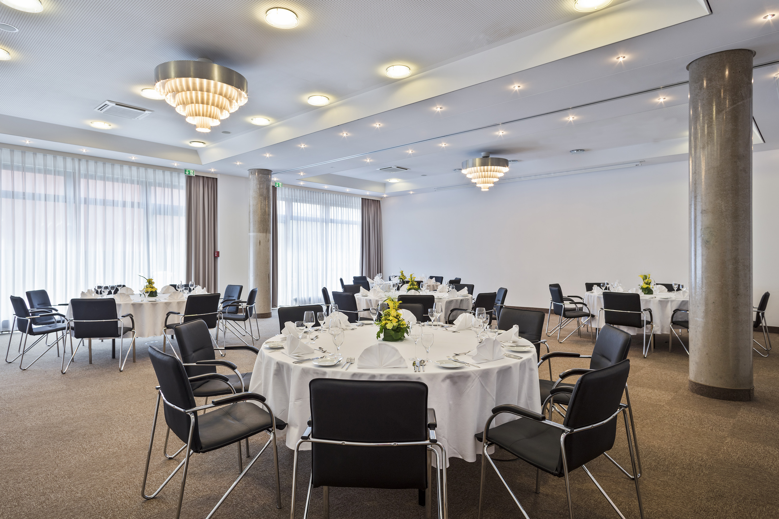 Modern conference room with set round tables, black chairs, and chandeliers.