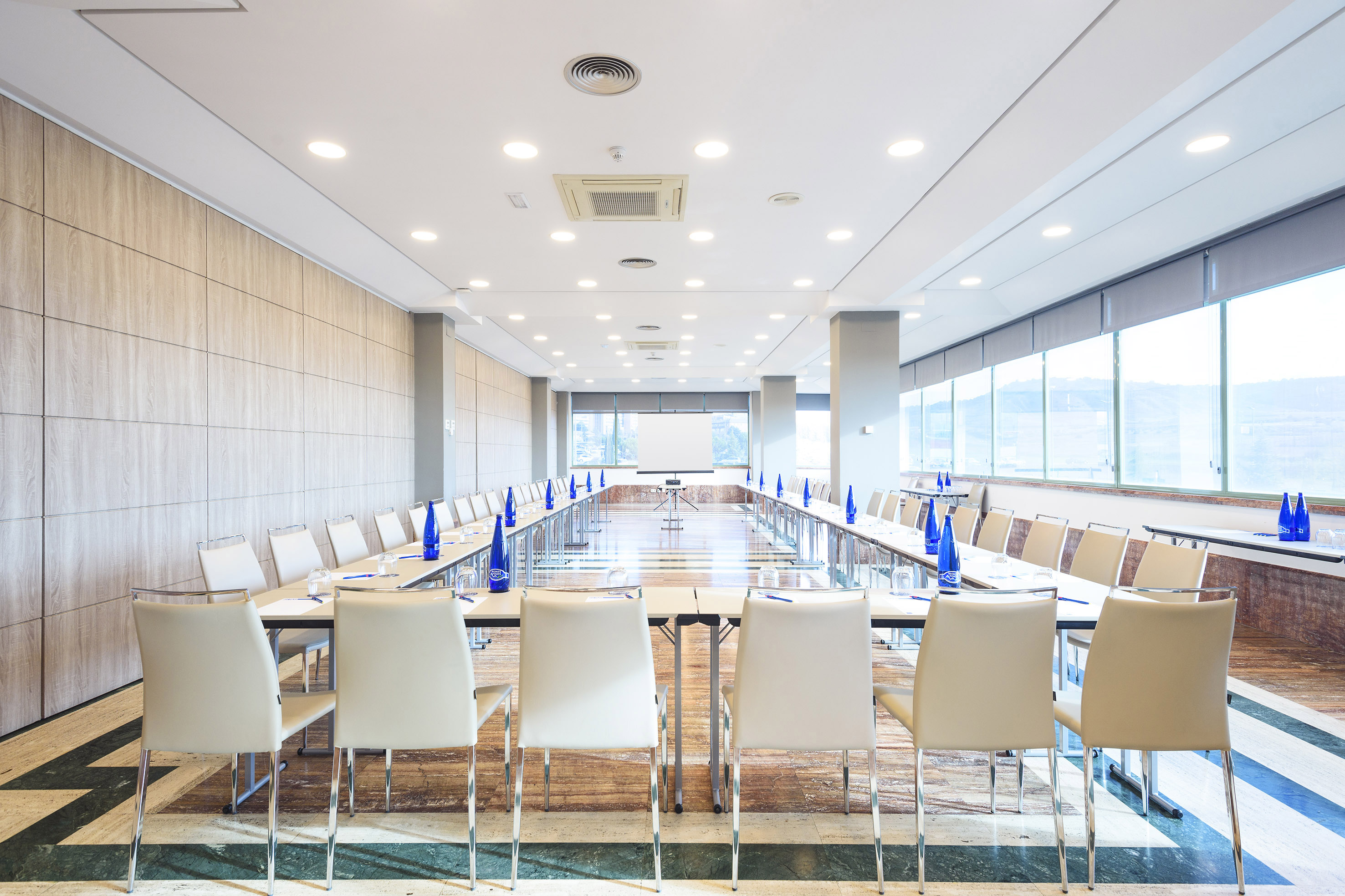 Modern meeting room with U-shape table setup, white chairs, and projector.