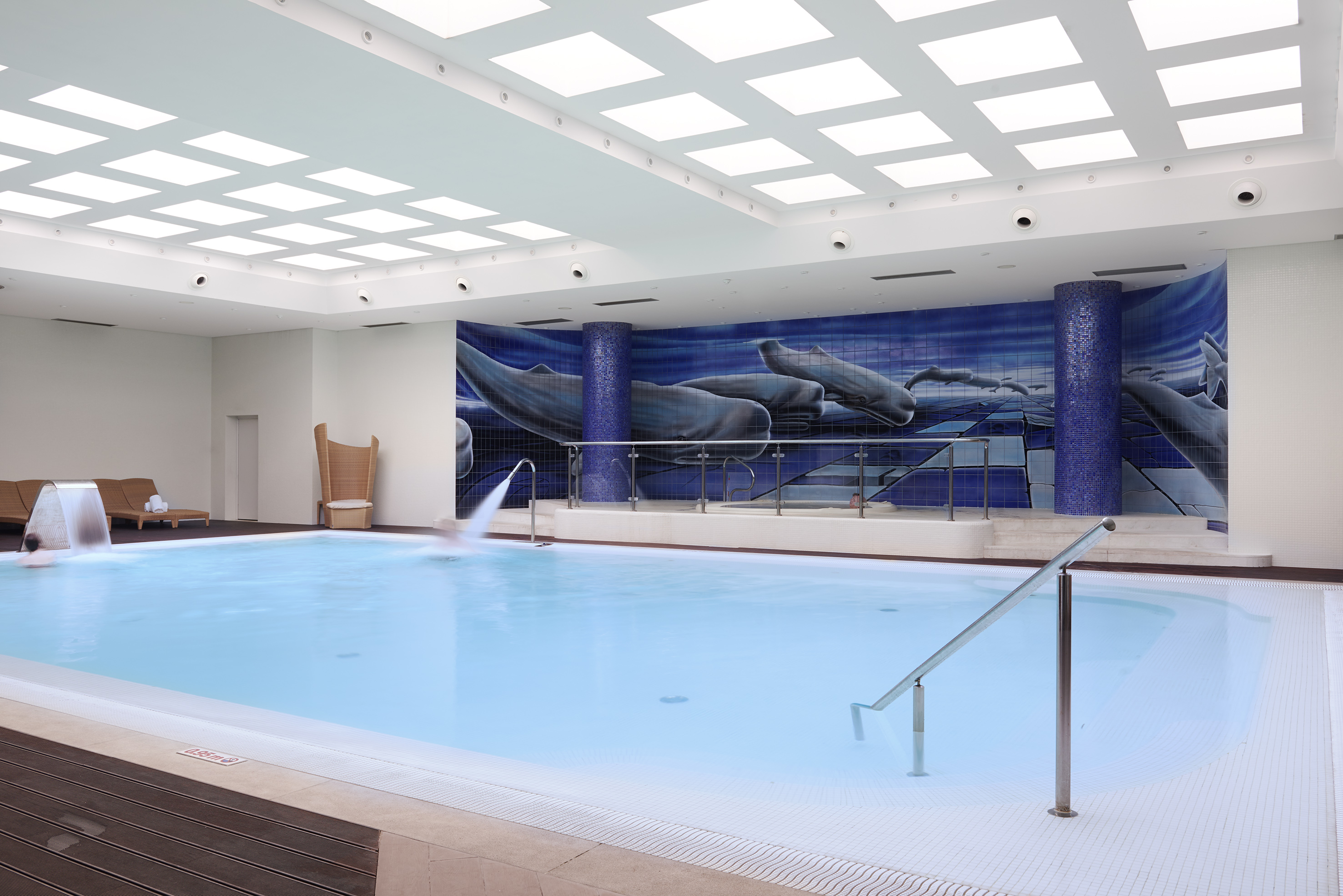 Indoor spa pool with blue whale mosaic wall and ceiling lights.