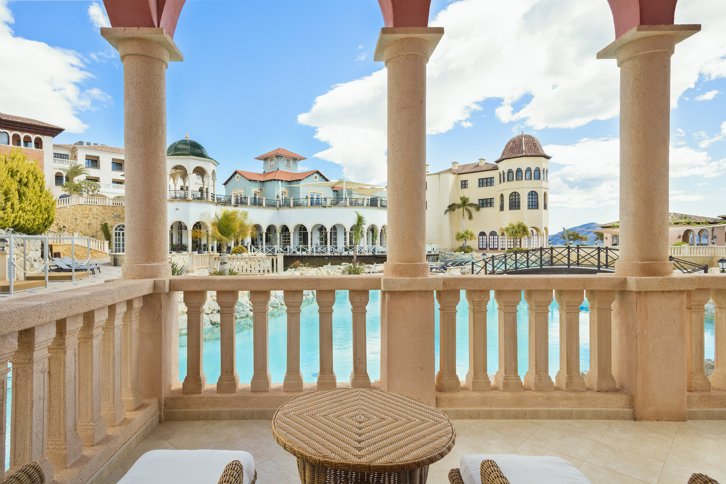 Luxury resort balcony overlooking a large pool with Mediterranean architecture.