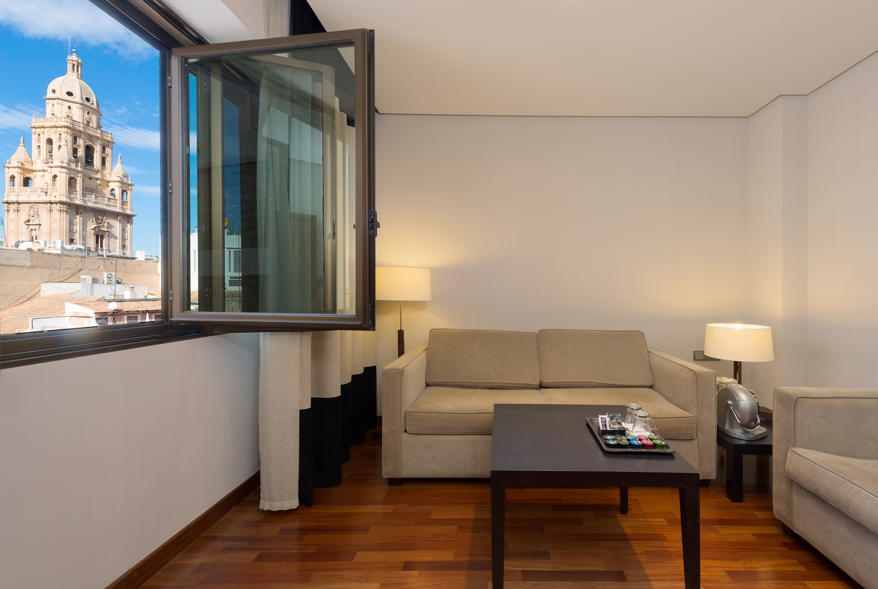 Hotel suite with living area and open window city view of a cathedral.