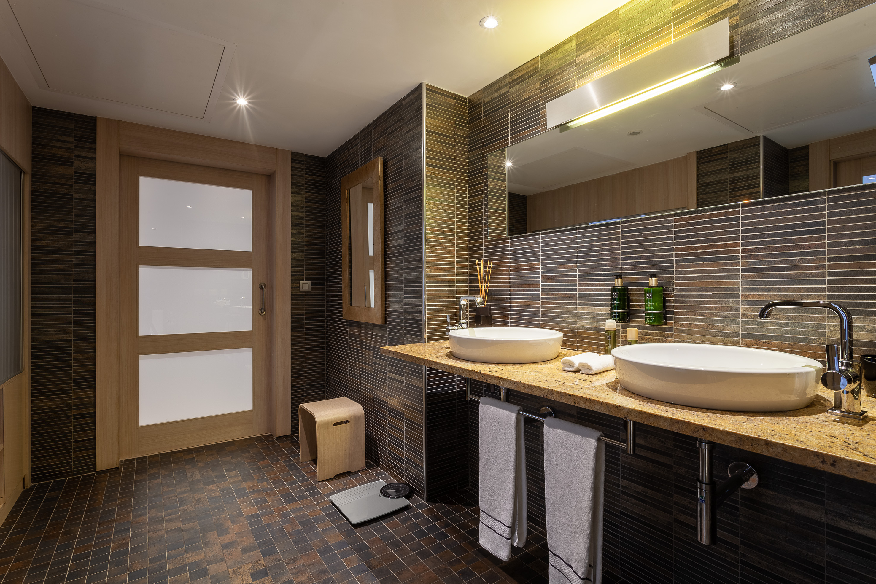 Modern bathroom with dual vessel sinks, granite counter, and brown mosaic tiles.