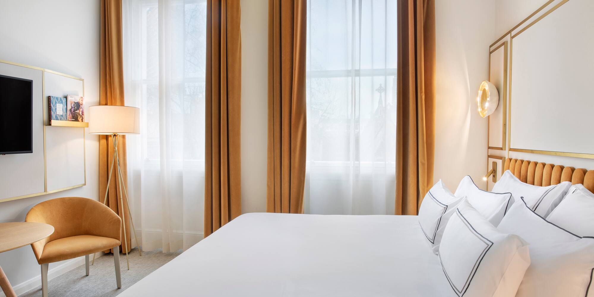 a bed with white sheets and a lamp in a room with curtains