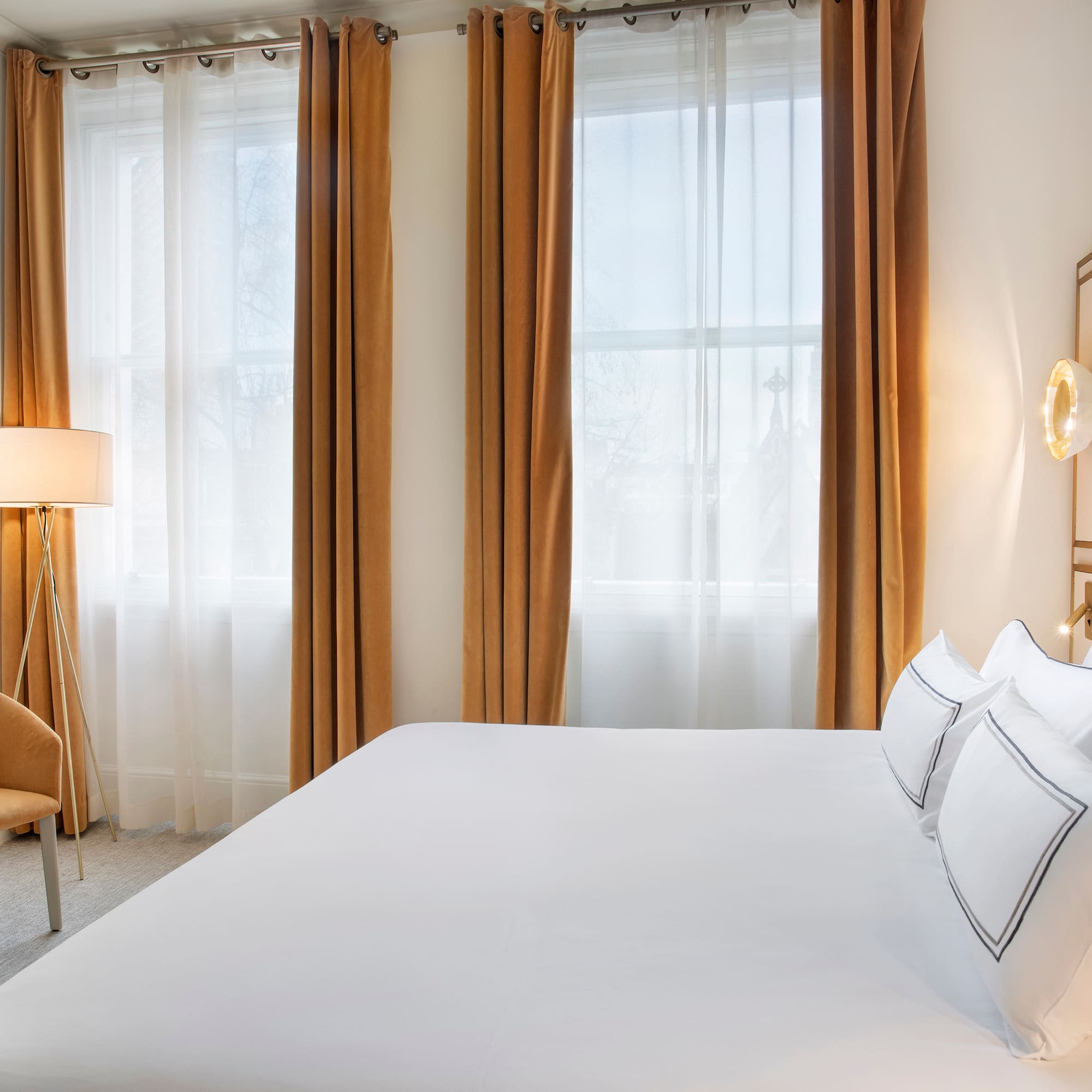 a bed with white sheets and a lamp in a room with curtains