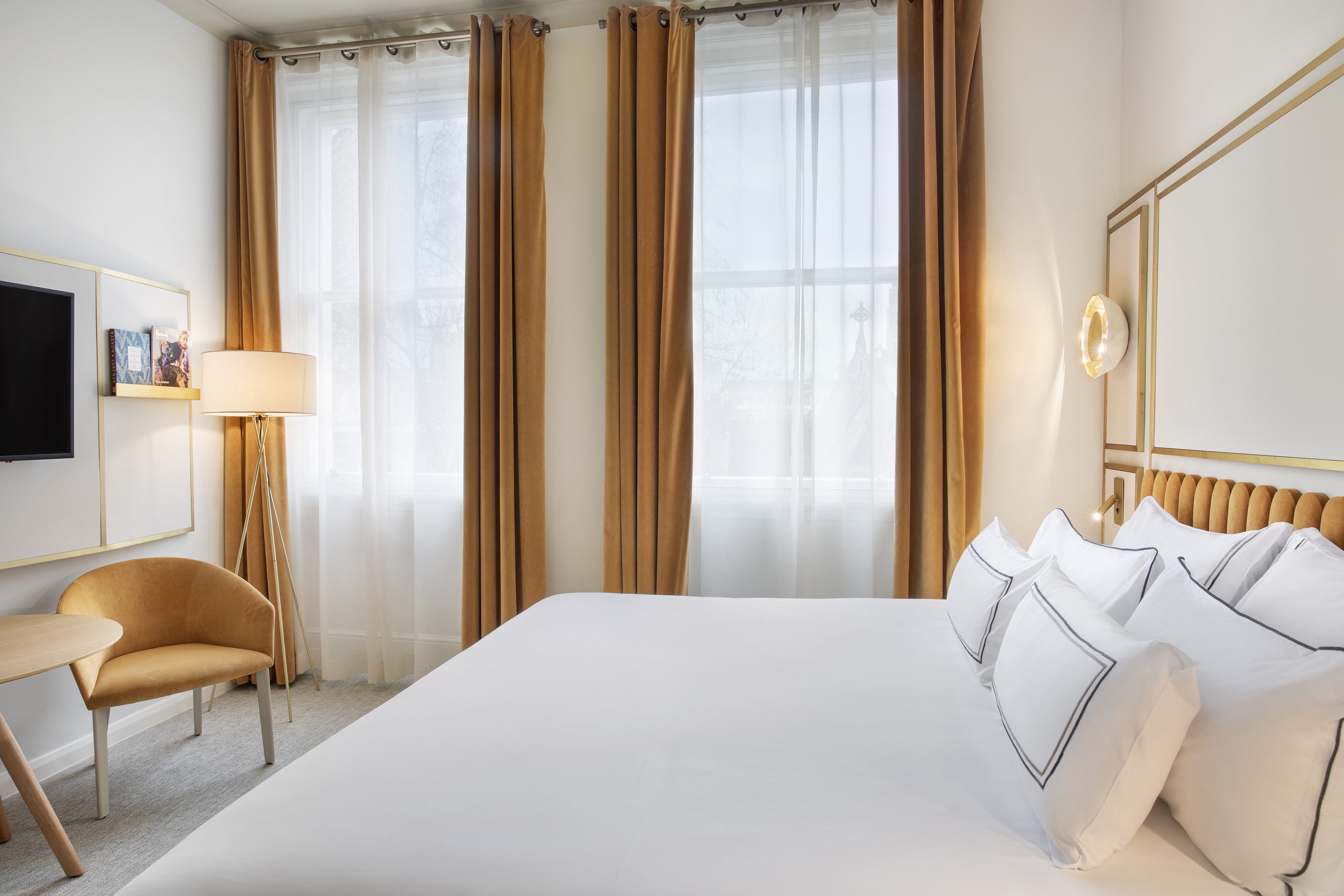 Modern hotel bedroom with king bed, golden headboard, and velvet curtains.