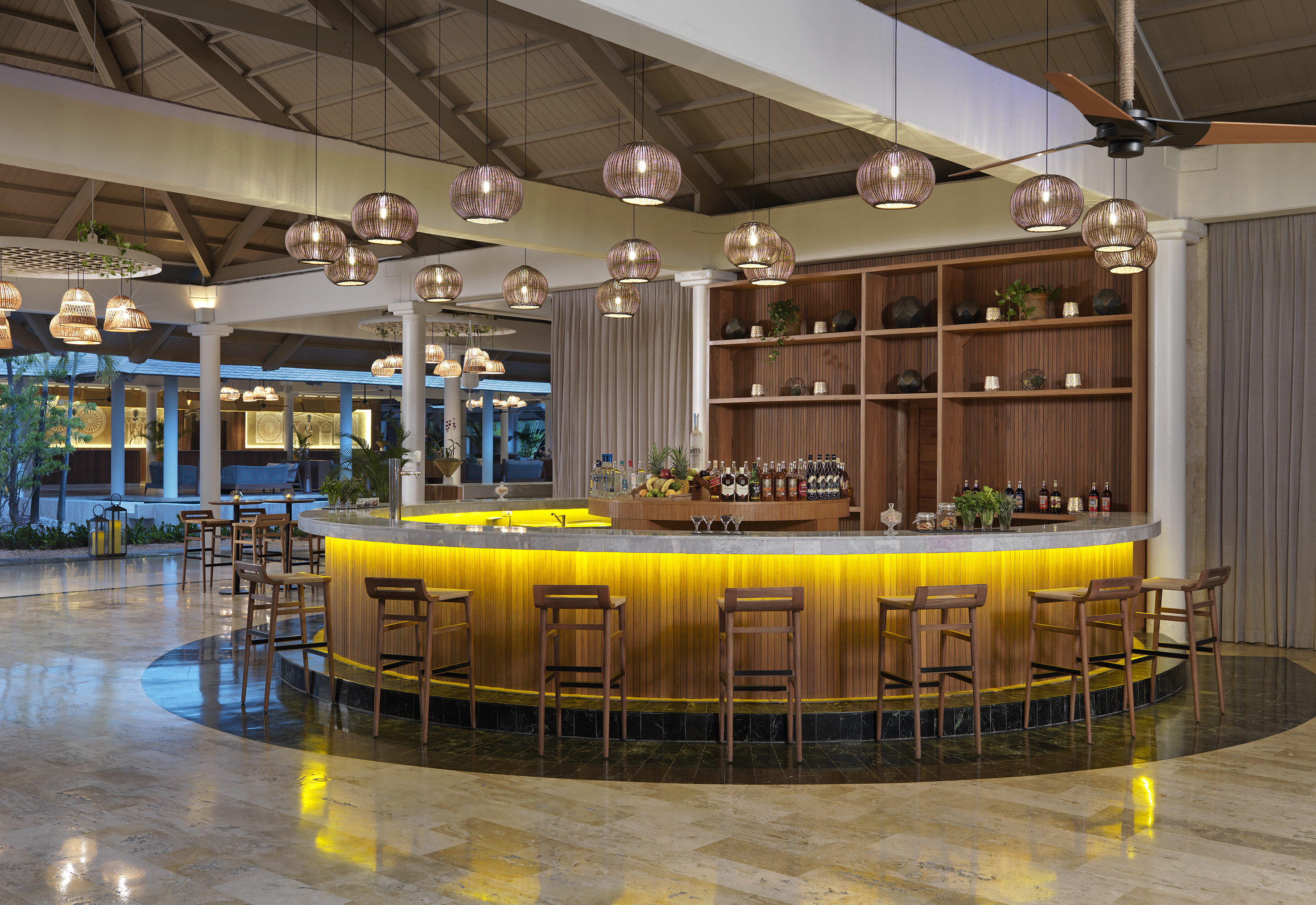 Hotel bar with illuminated counter, wooden stools, and woven pendant lights.