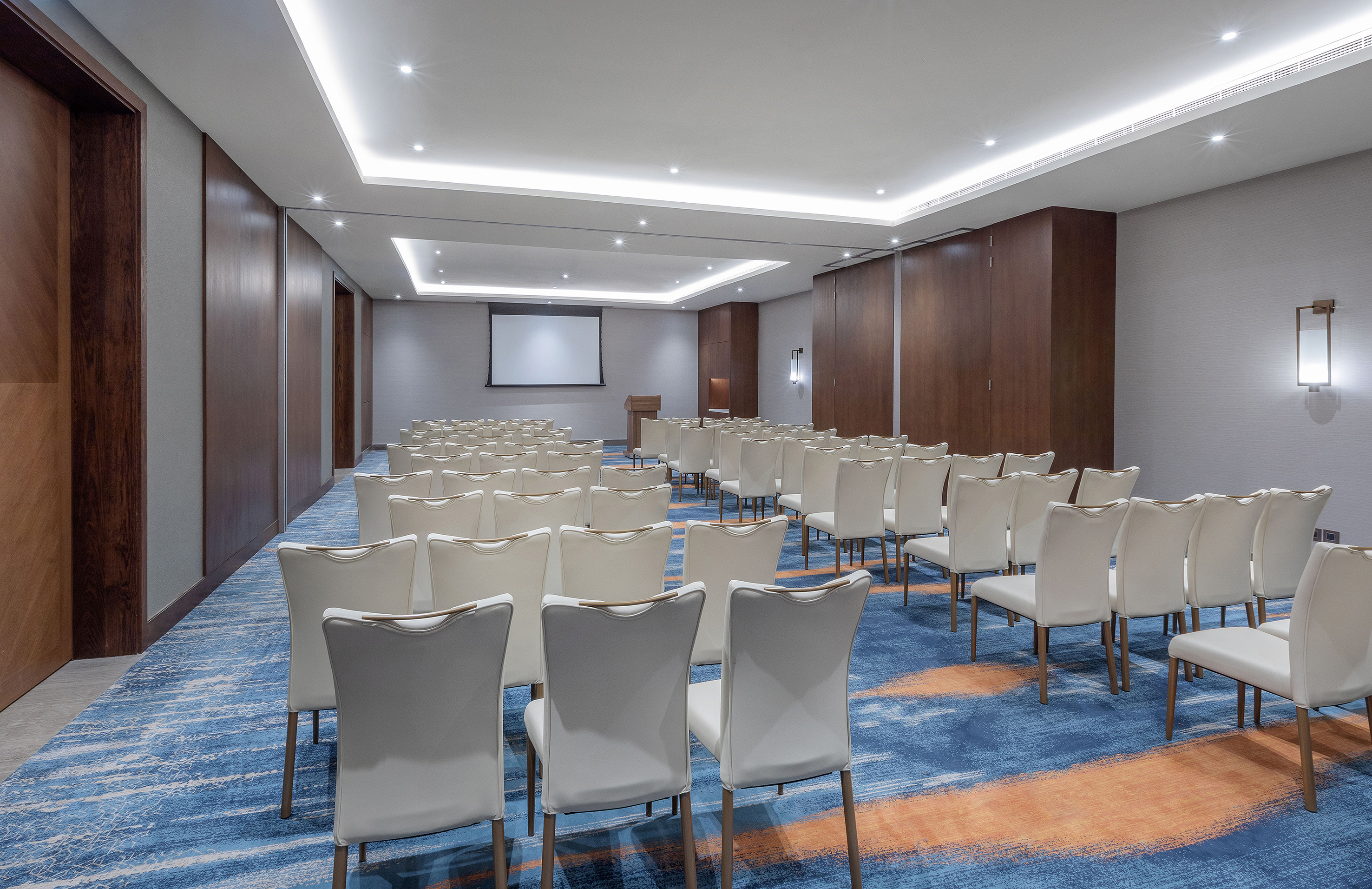 Modern meeting room with white chairs, projection screen, and podium.