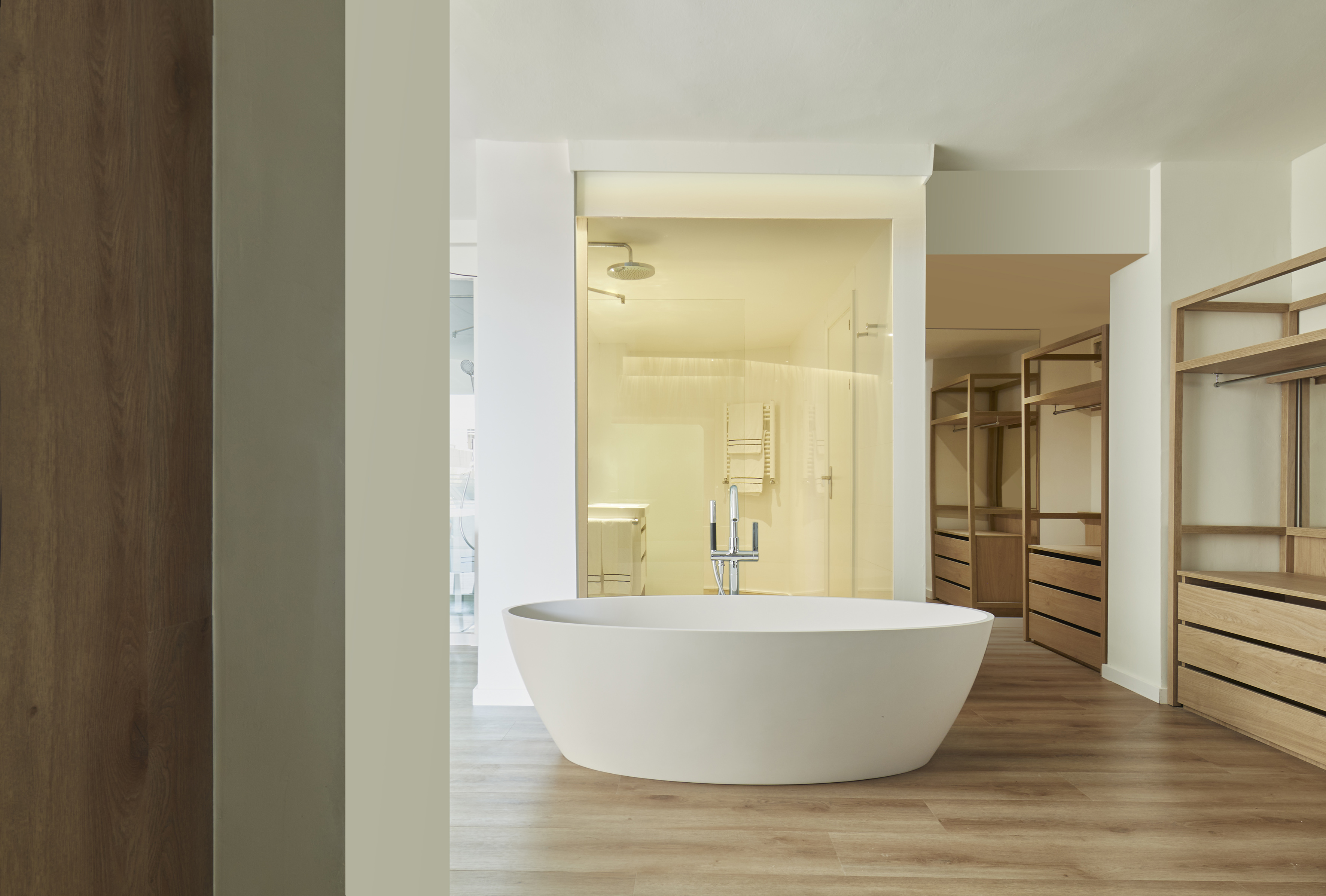 Modern bathroom with freestanding tub, glass shower, and open wood closet.