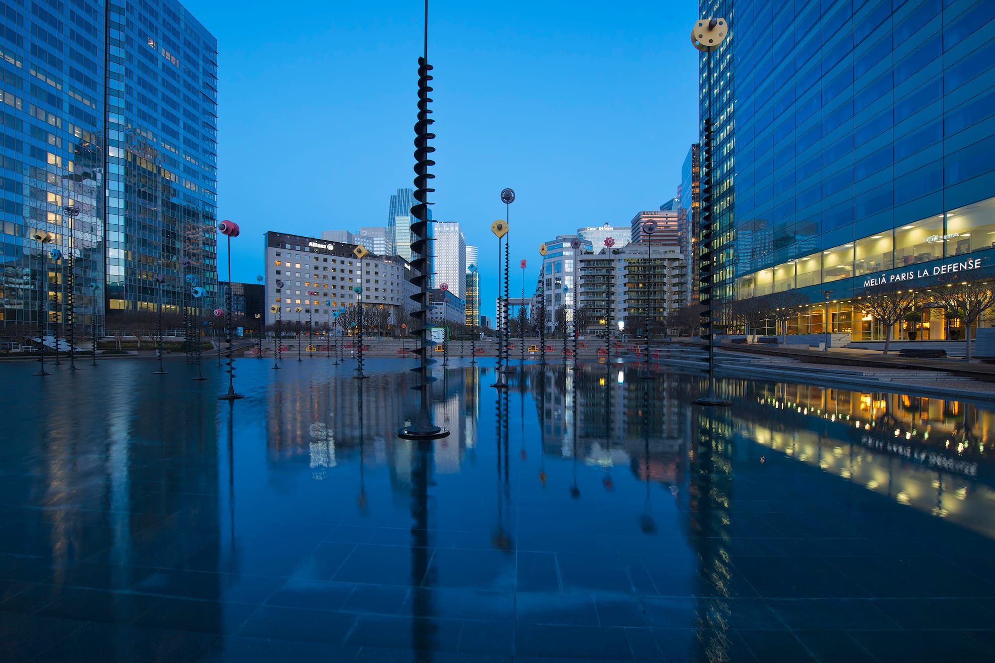 La Défense Paris cityscape at dusk, reflecting skyscrapers and water art.