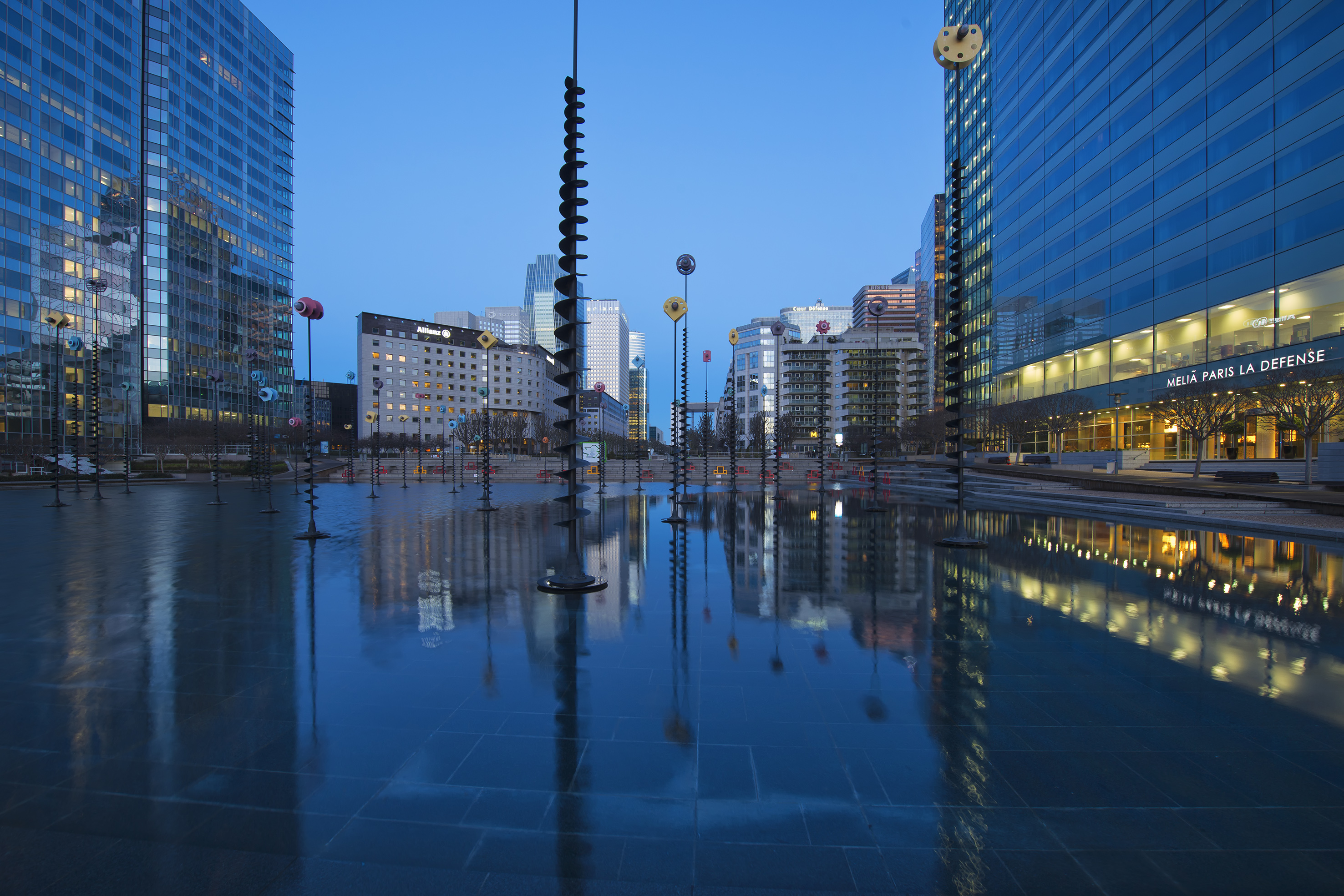 La Défense Paris cityscape at dusk, reflecting skyscrapers and water art.