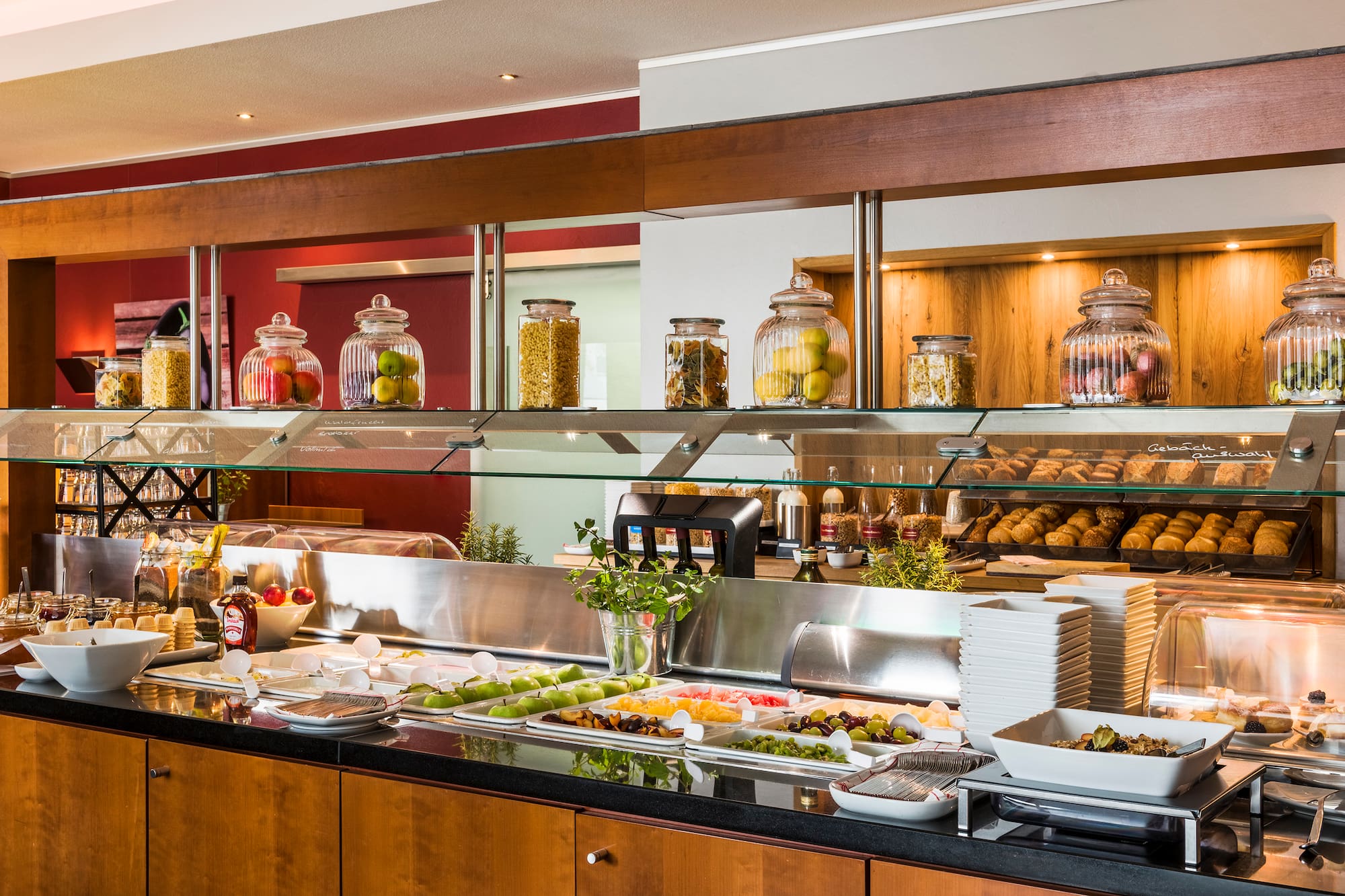 Breakfast buffet with fresh fruit, baked goods, and cereals in glass jars.