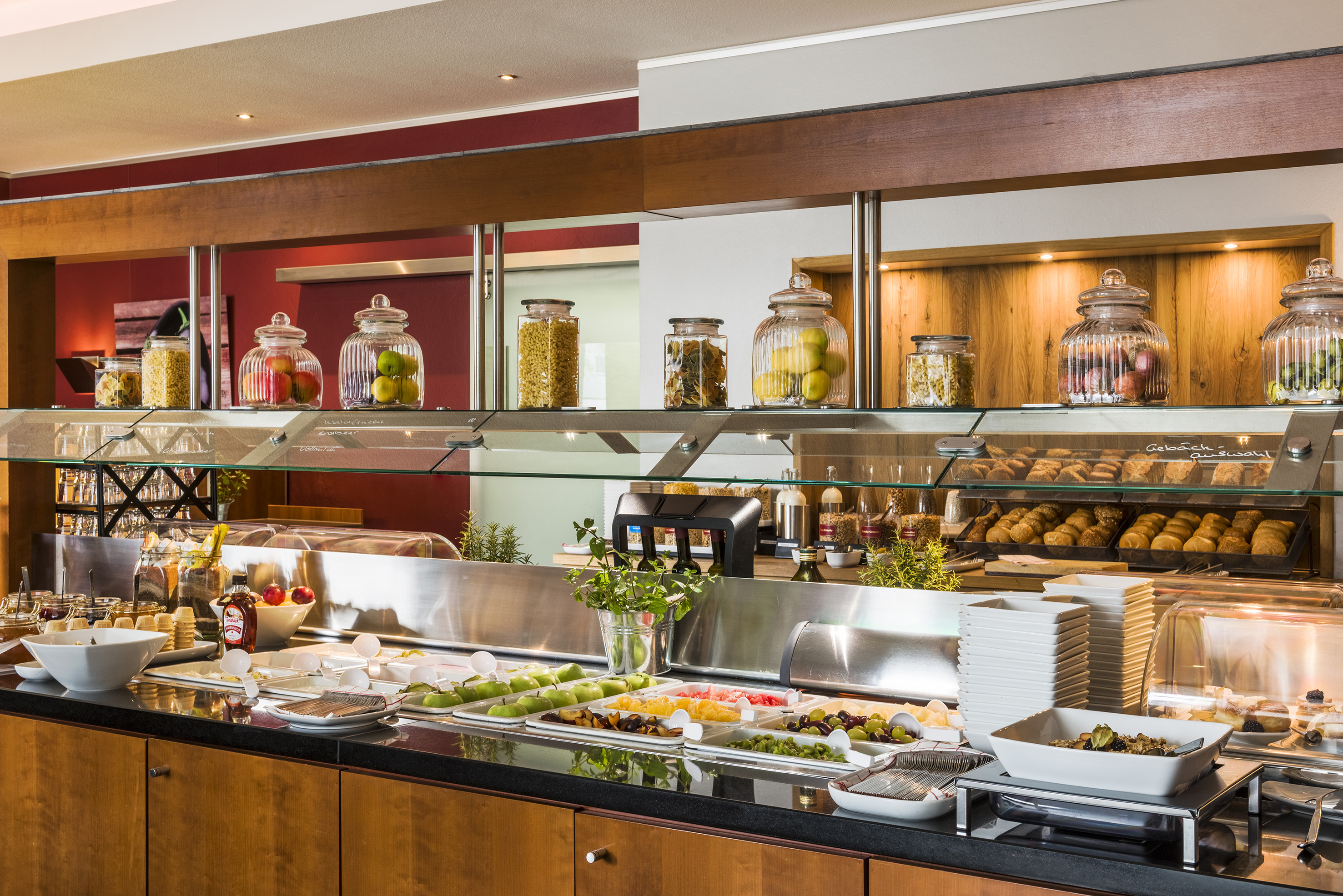 Breakfast buffet with fresh fruit, baked goods, and cereals in glass jars.