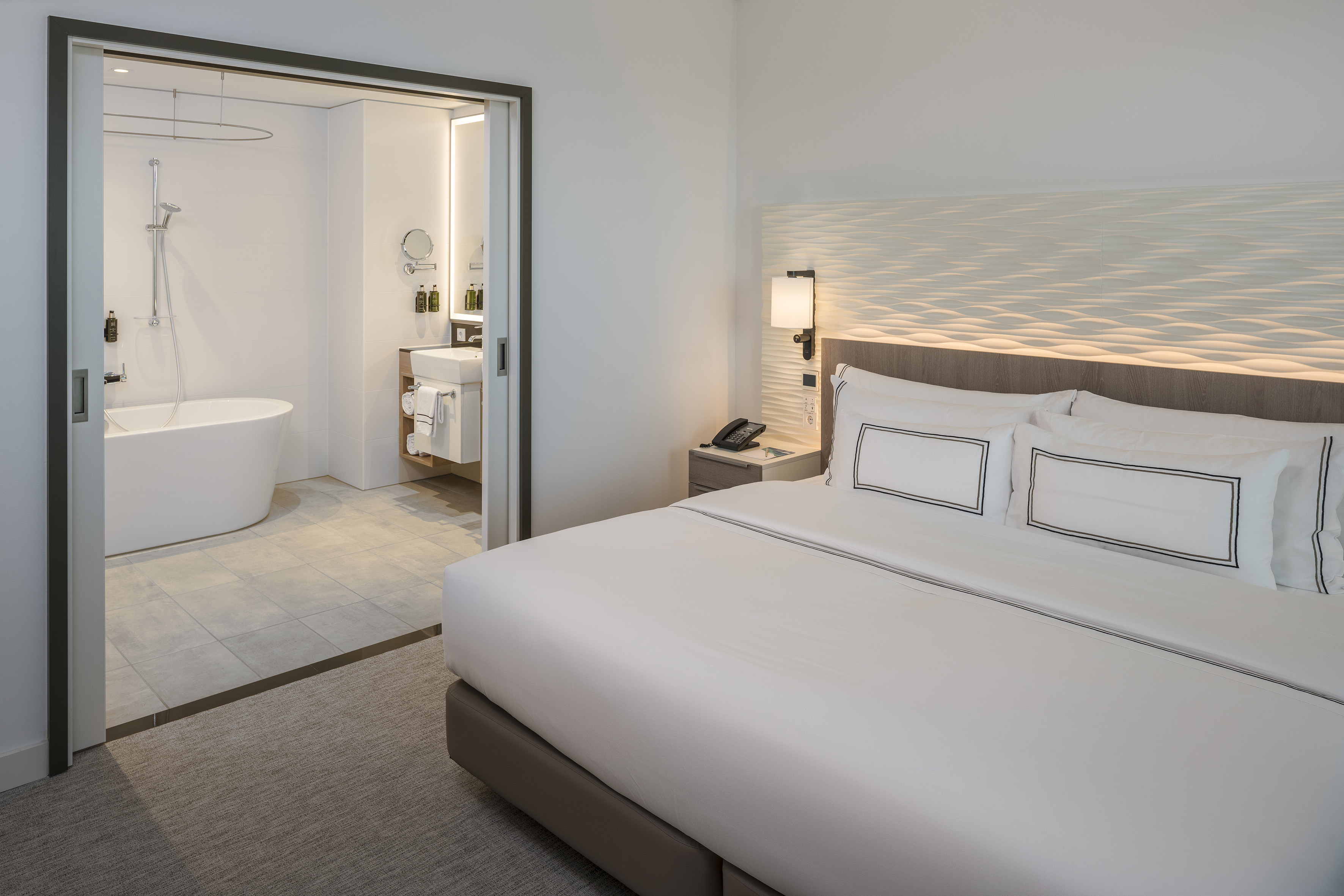 Luxury hotel room with king bed, illuminated headboard, and modern bathroom.