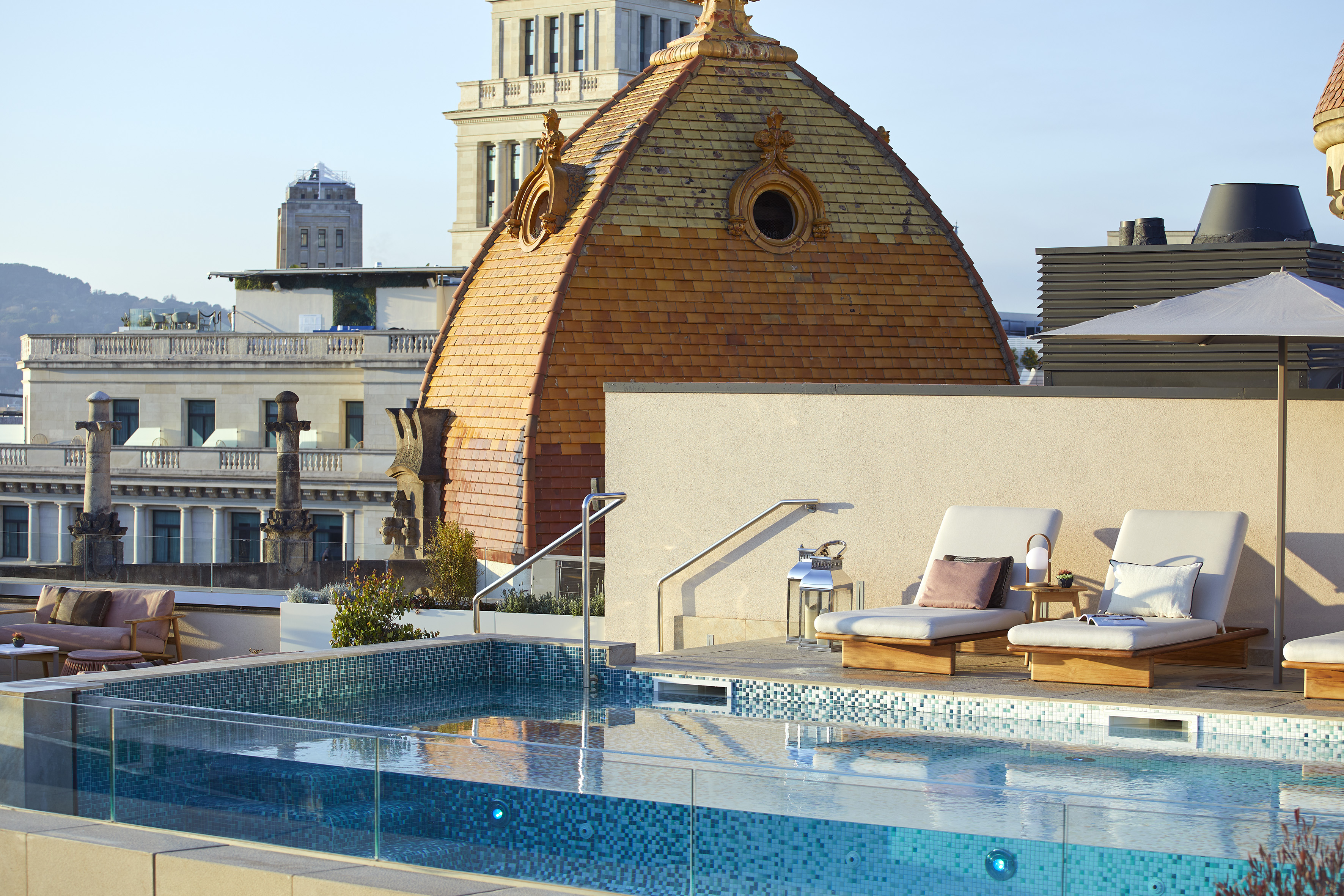 Sunny rooftop infinity pool with lounge chairs and historic domed building.