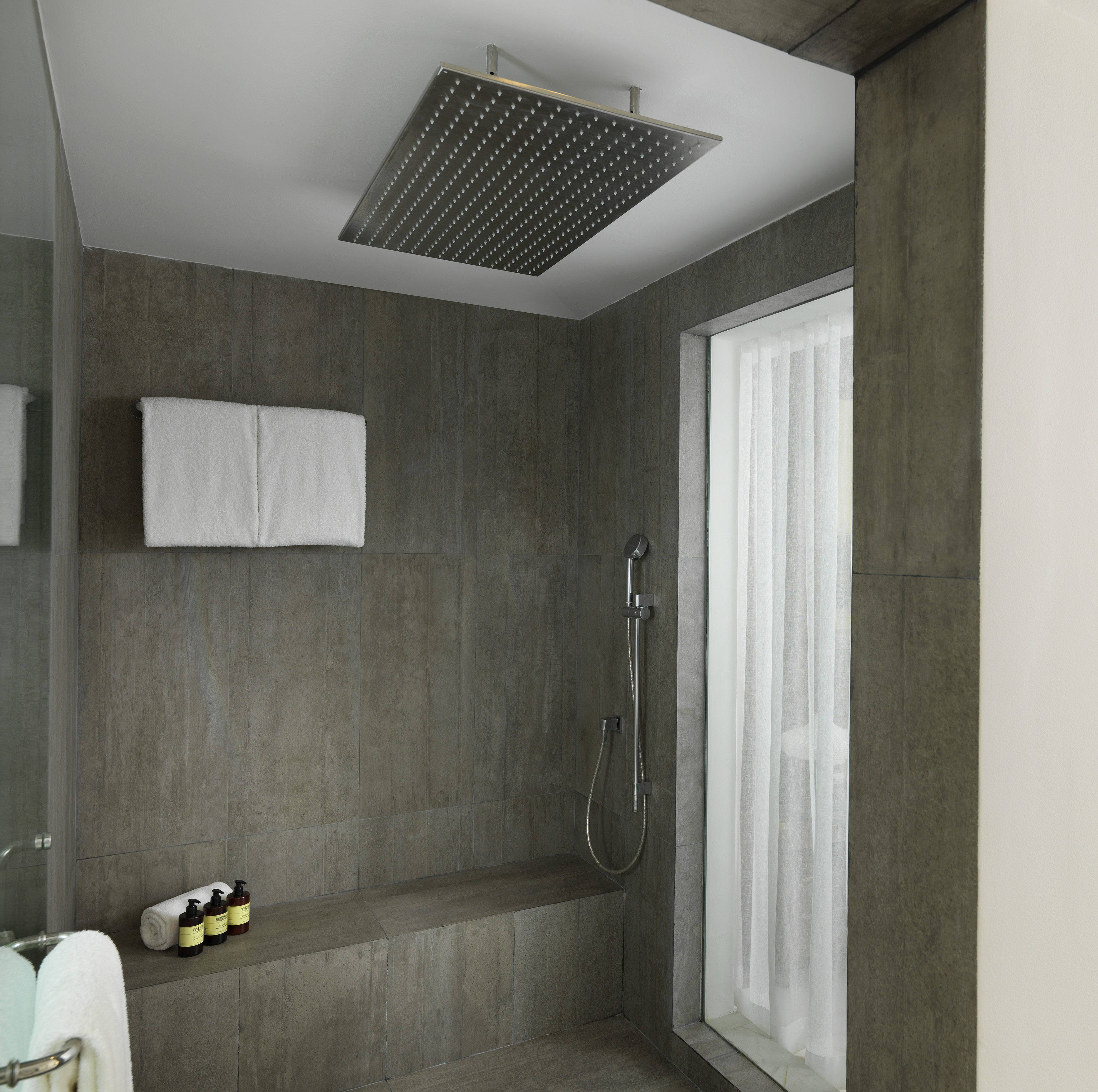 Modern gray tiled shower with rainfall head, built-in bench, and white towels.