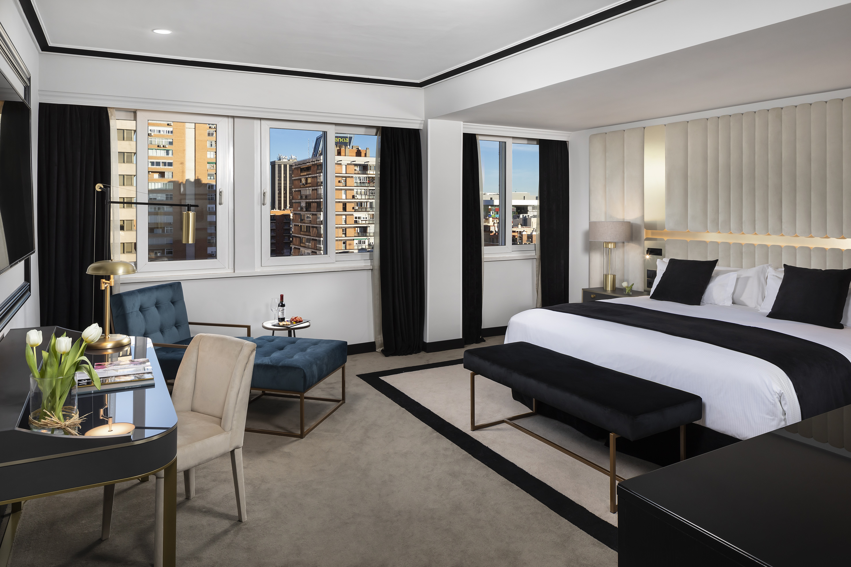 Modern hotel suite with king bed, city view windows, and stylish furnishings.