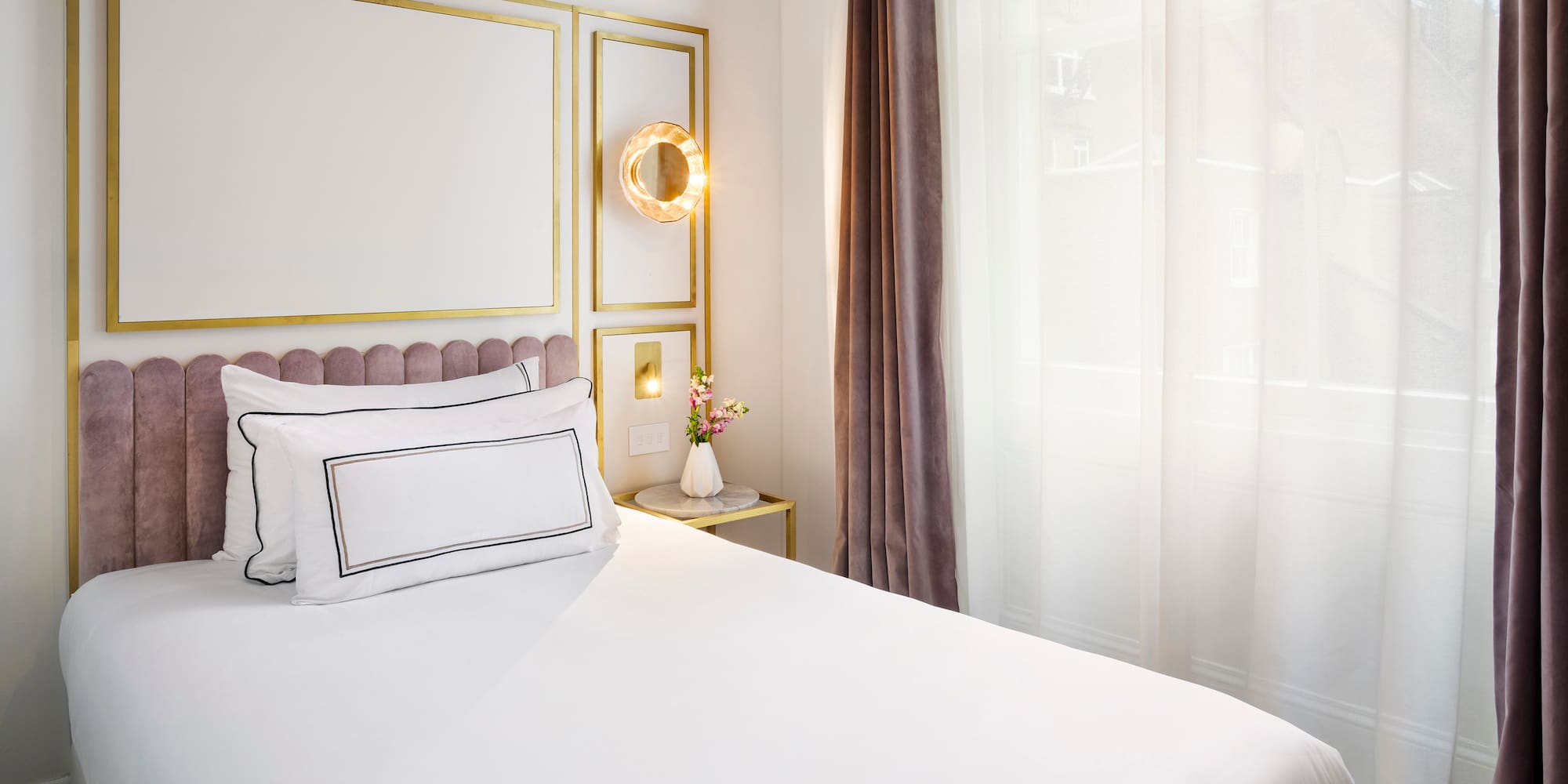 a bed with white sheets and pillows in a room with curtains