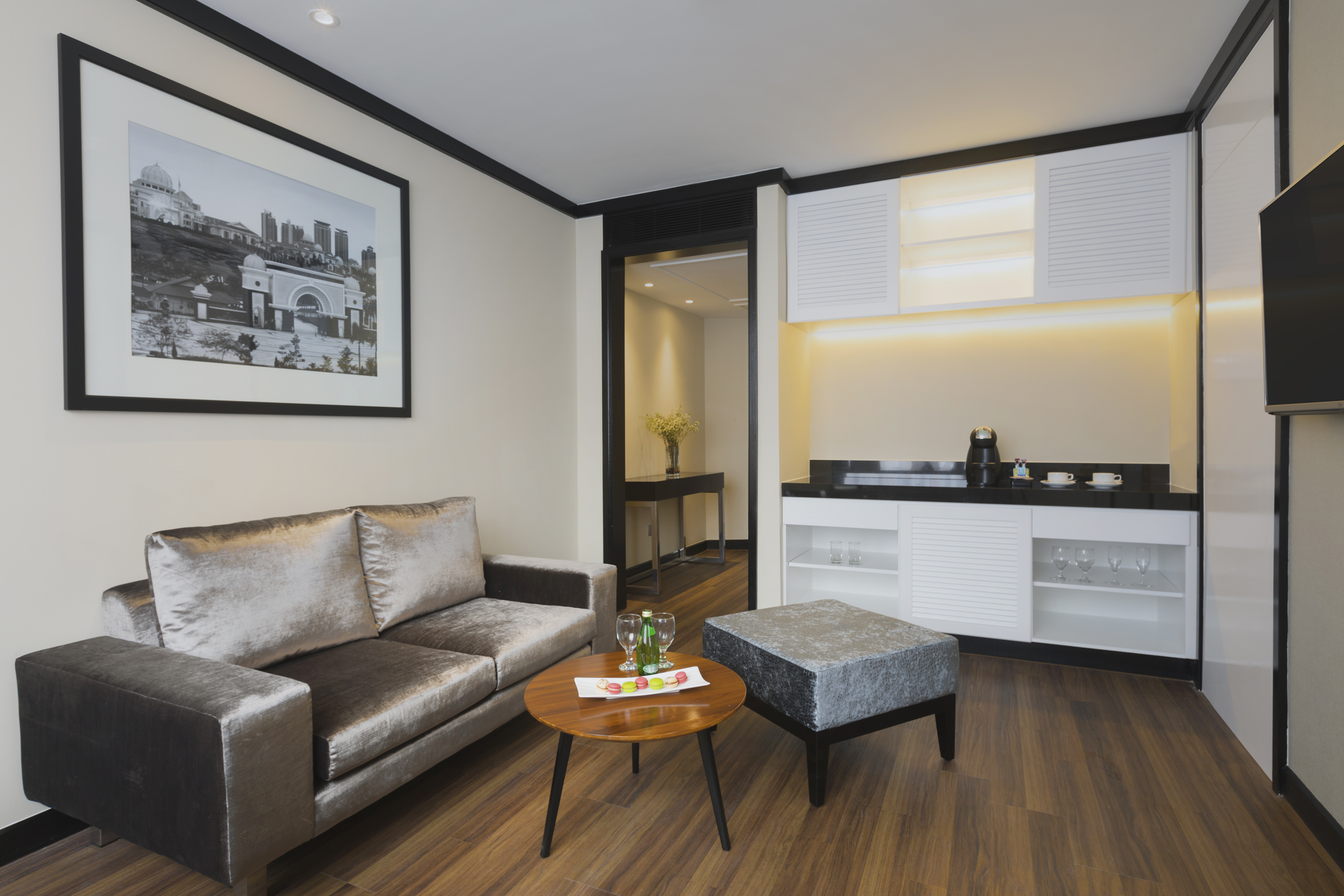 Modern hotel suite living area with gray sofa, coffee table, and kitchenette.