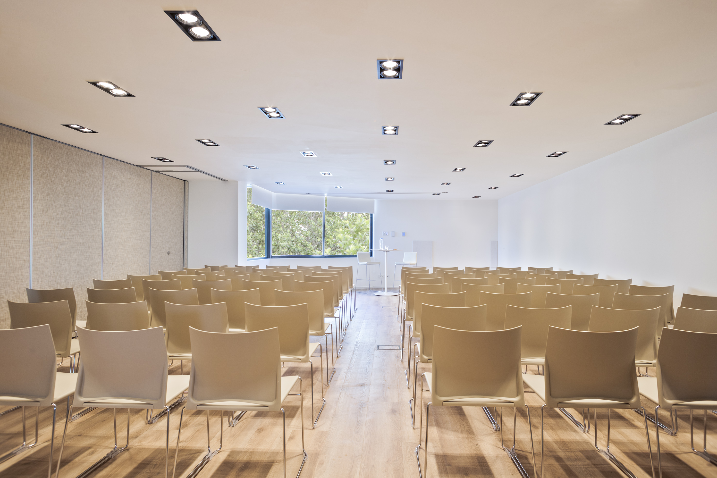 Empty modern event space with chairs, wood floor, and large windows.