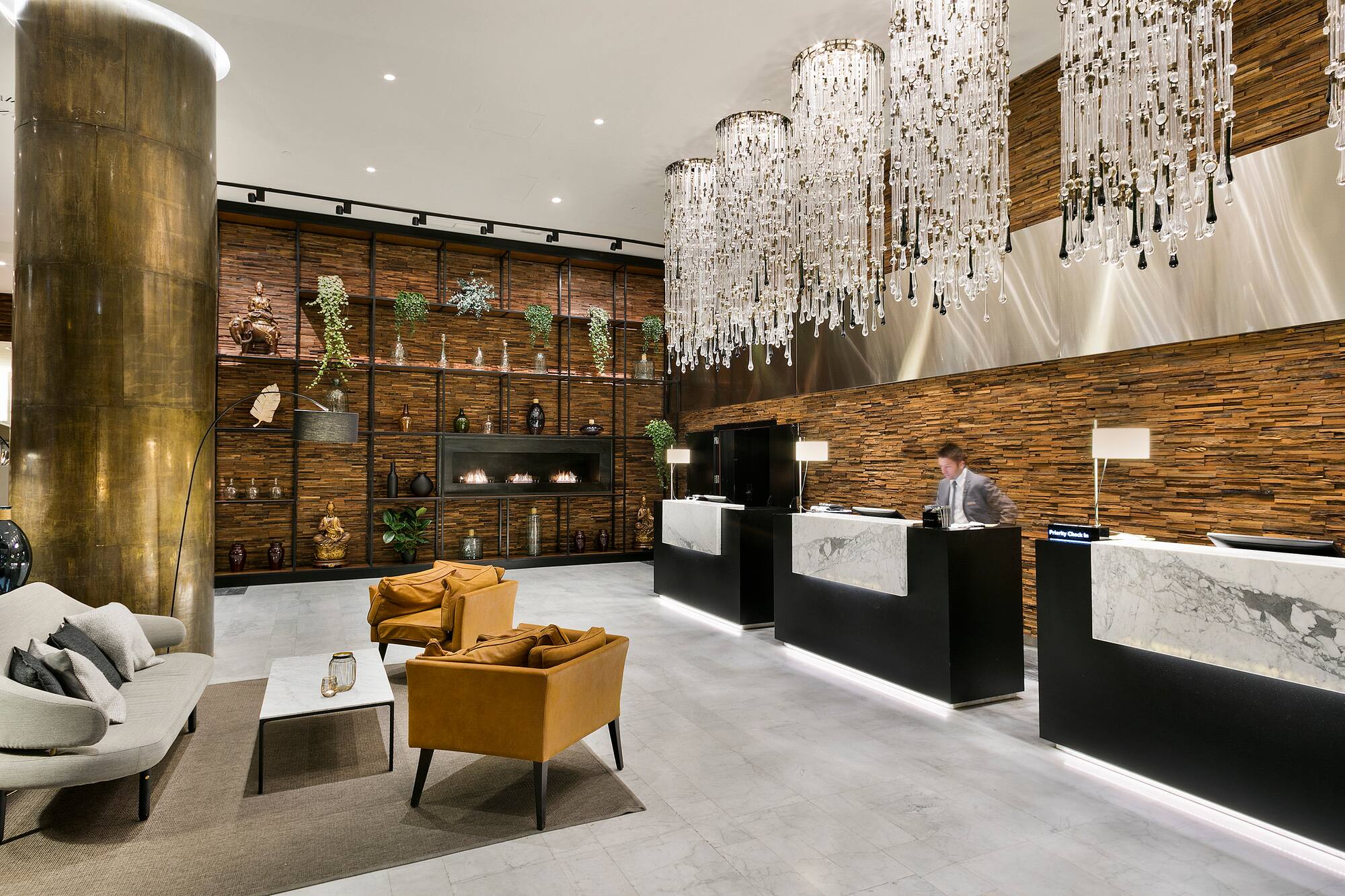 Modern hotel lobby with crystal chandeliers, wood paneling, and reception desk.