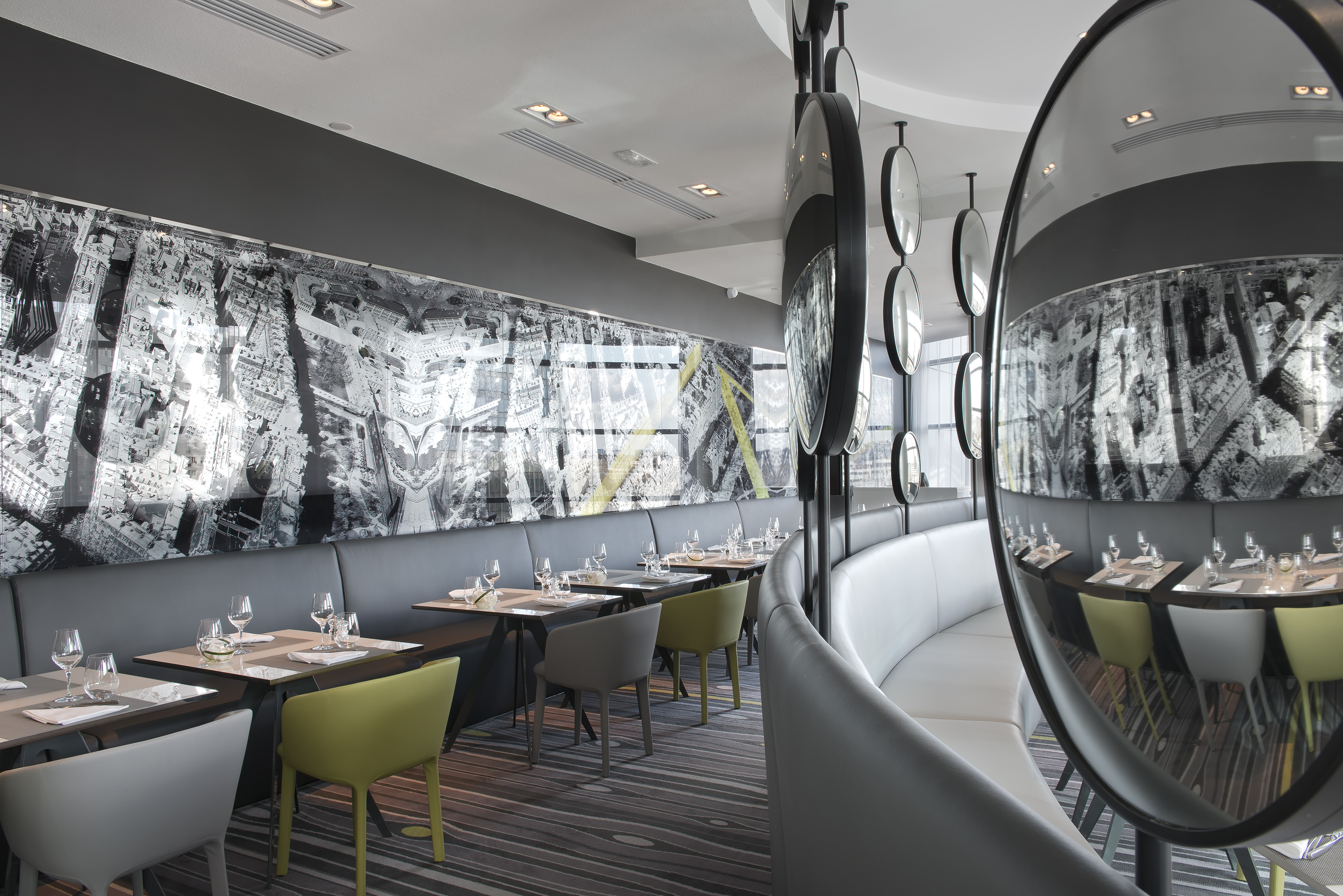 Modern restaurant interior with cityscape mural, curved booth, and set tables.