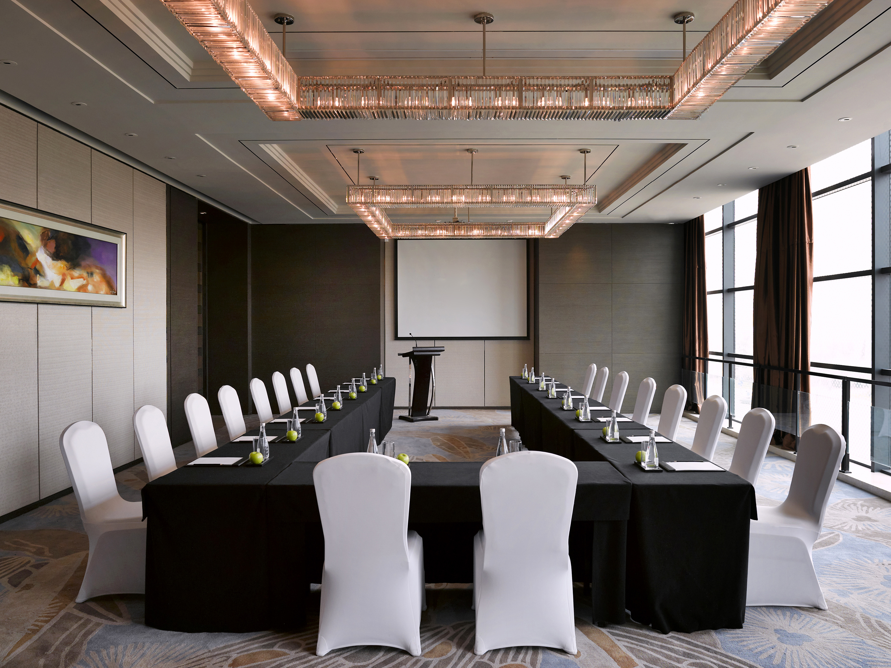 Modern conference room with U-shaped table, white chairs, projector, chandeliers.