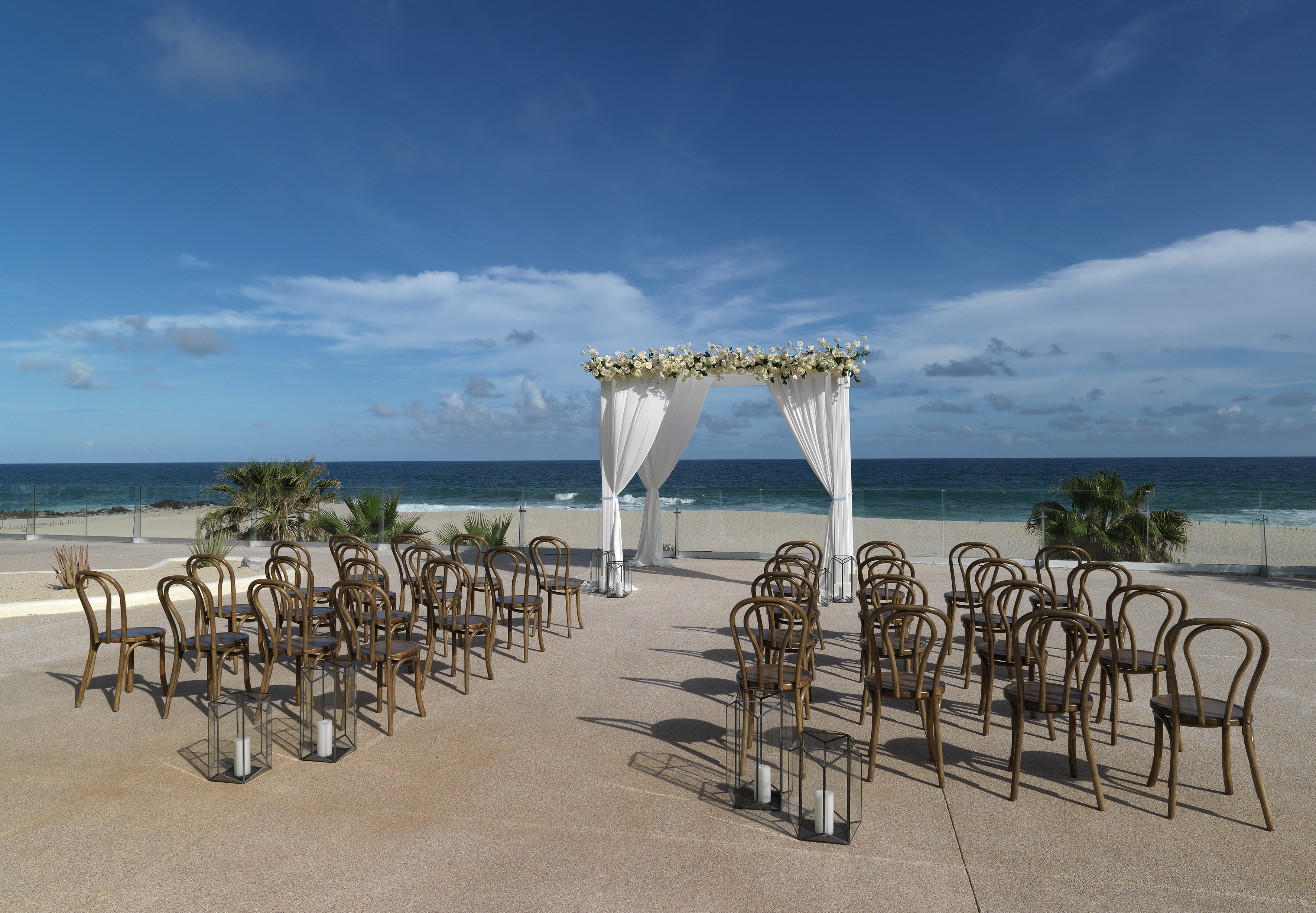 Elegant beach wedding setup with floral arch, guest chairs, and ocean backdrop.