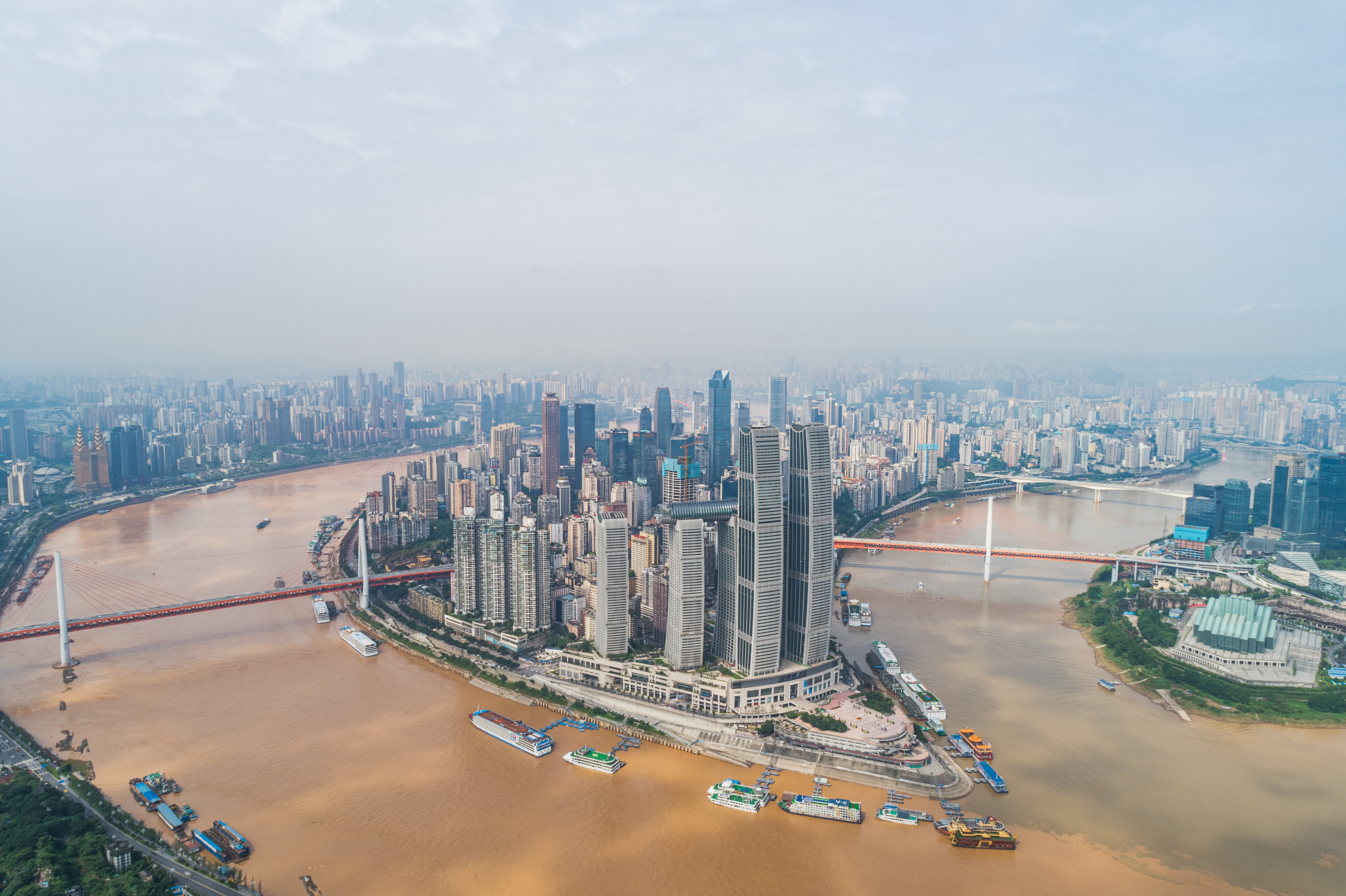 Aerial view of Chongqing city skyline with dense high-rises, muddy rivers, and bridges.