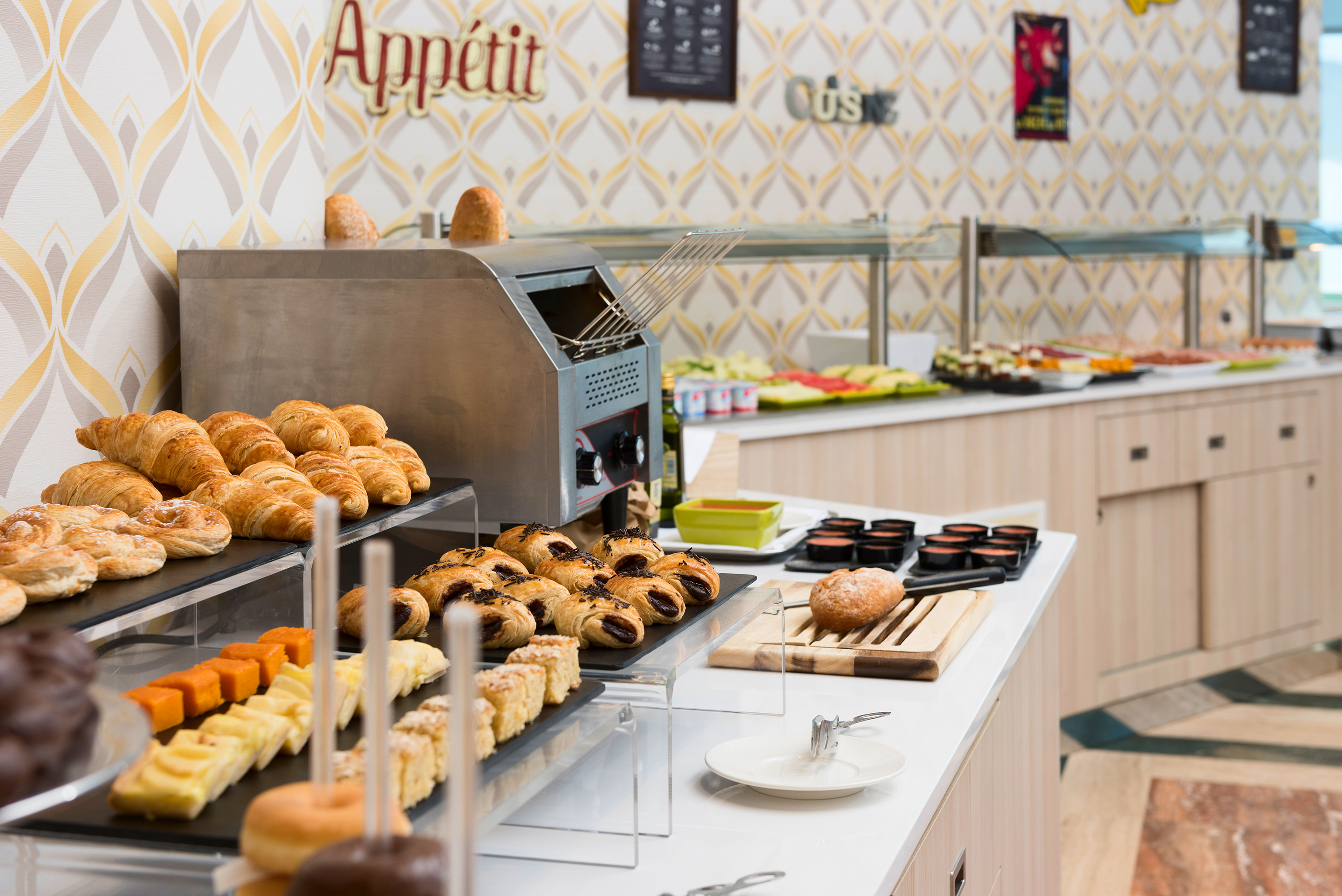 Hotel breakfast buffet with fresh croissants, pastries, bread, fruit, and toaster.