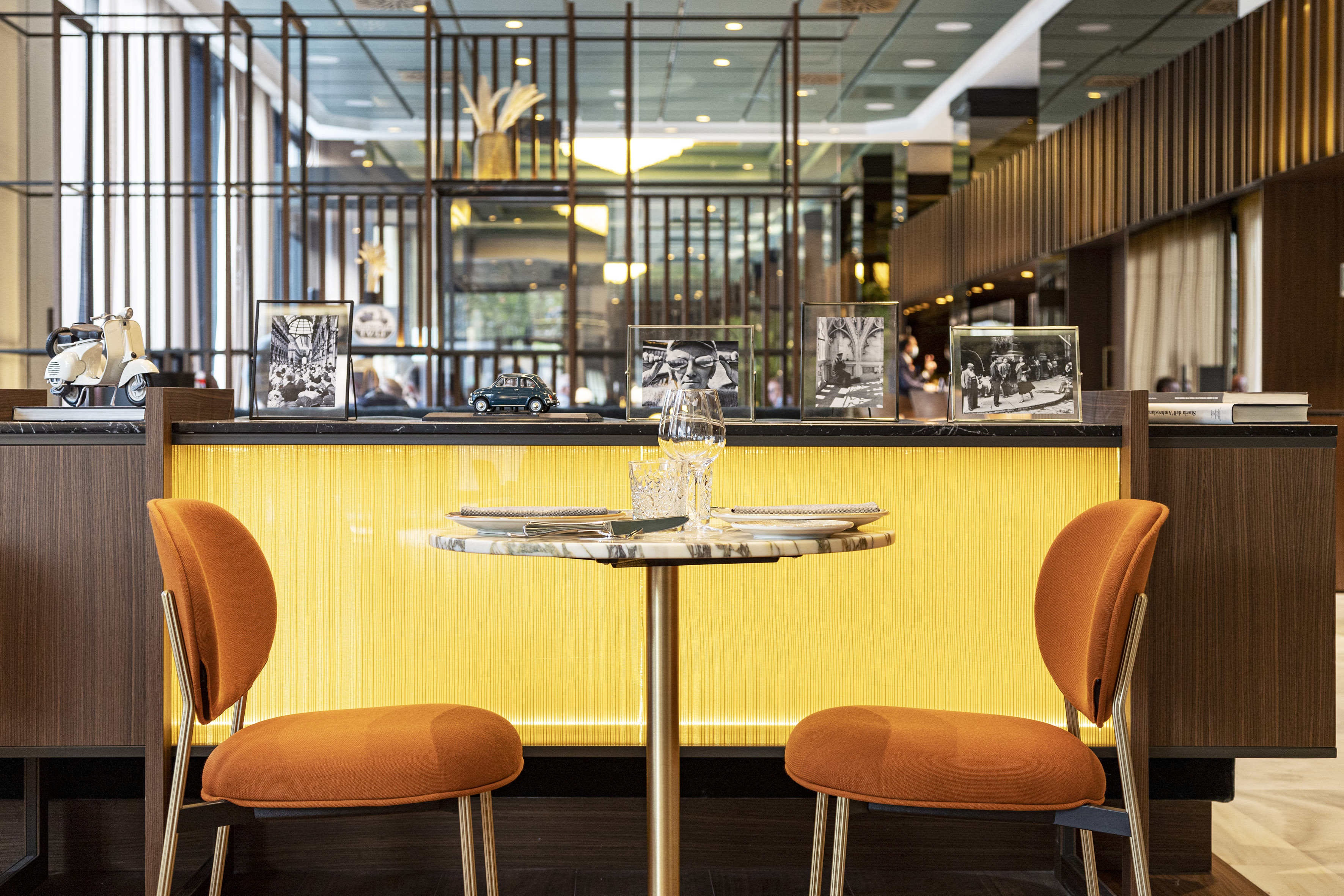 Modern hotel lounge dining area with orange chairs and decorated bar.