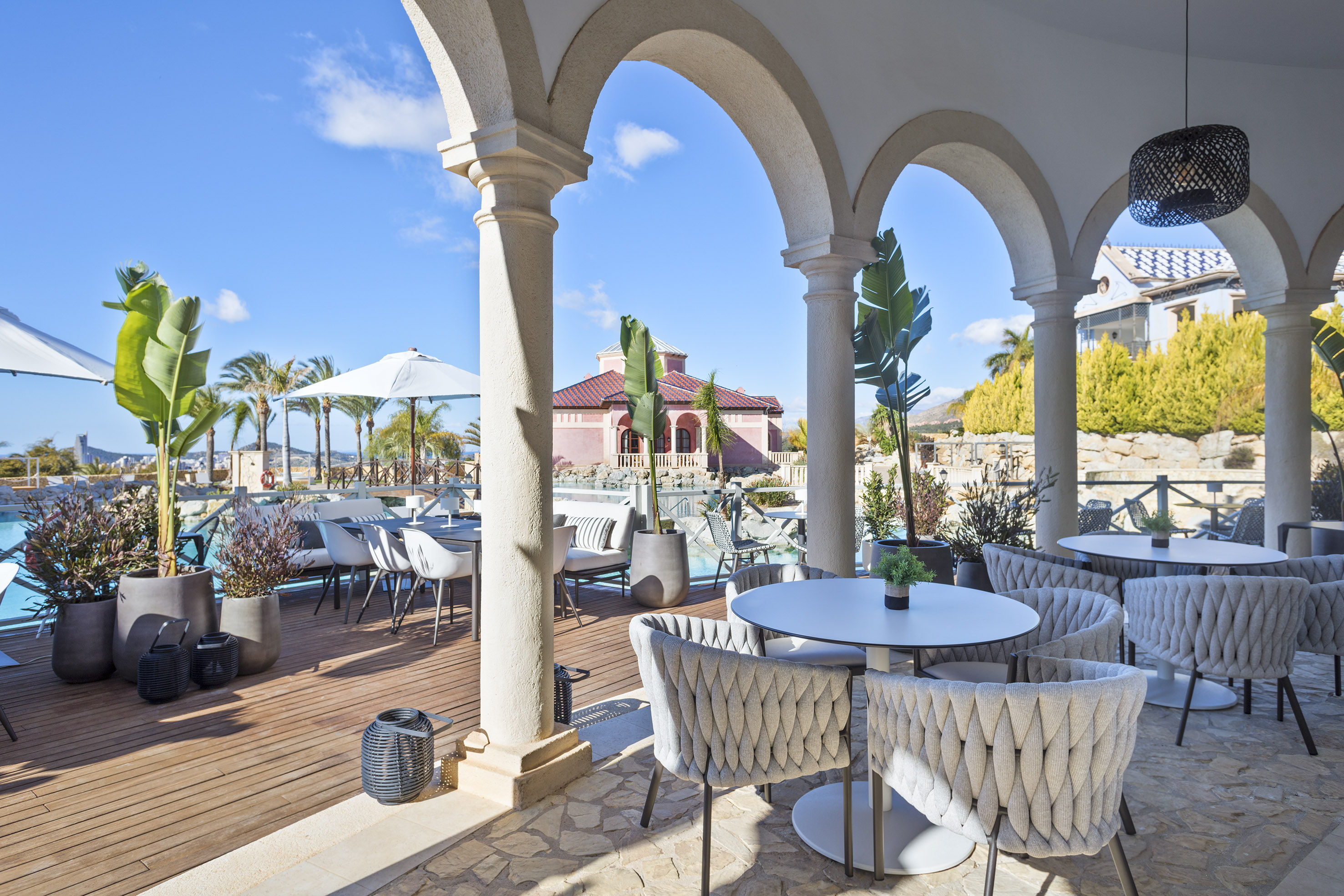 Luxury resort patio with arched columns, modern seating, and pool view.