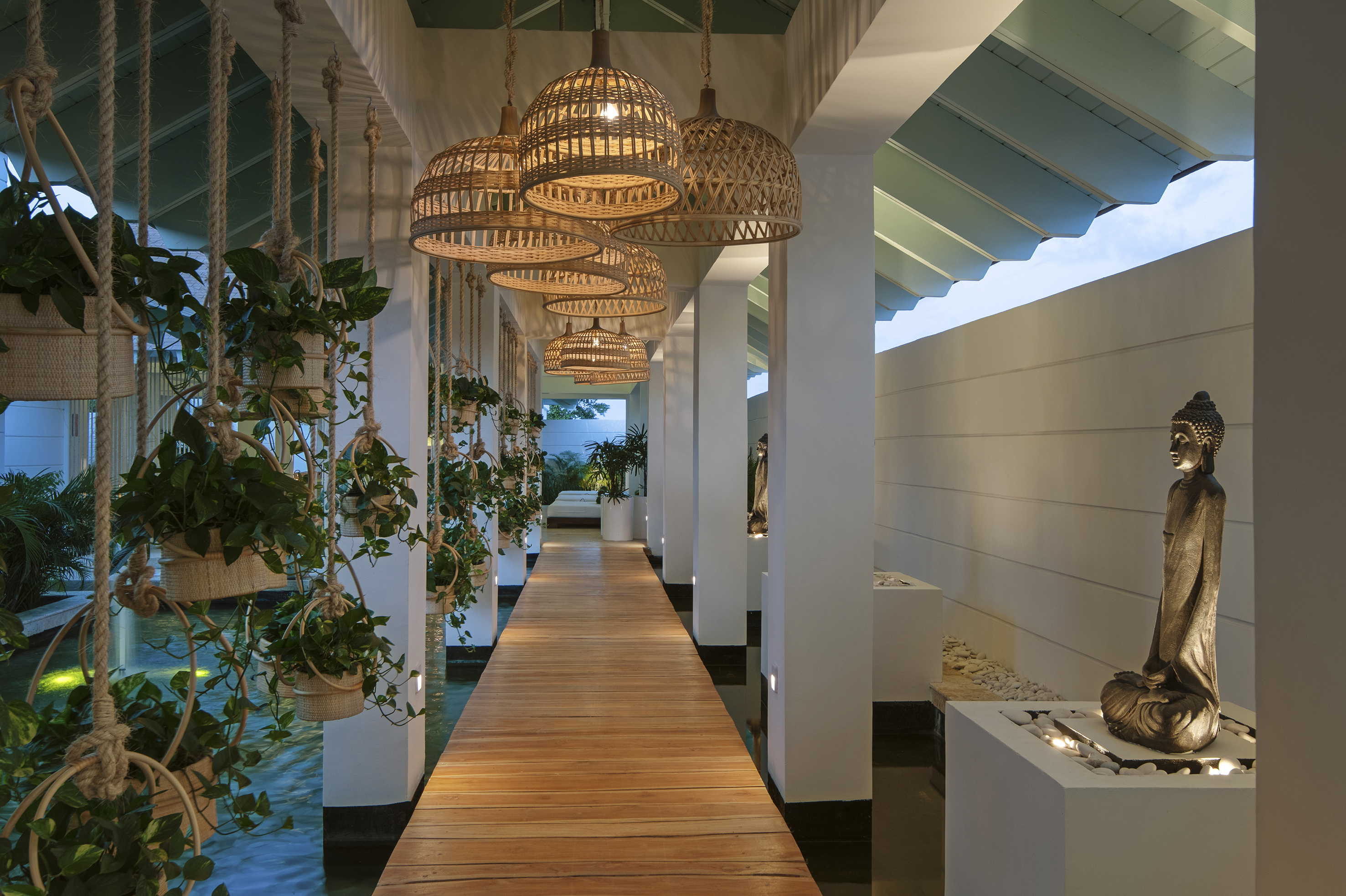 Tranquil spa pathway with hanging plants, rattan lights, and Buddha.