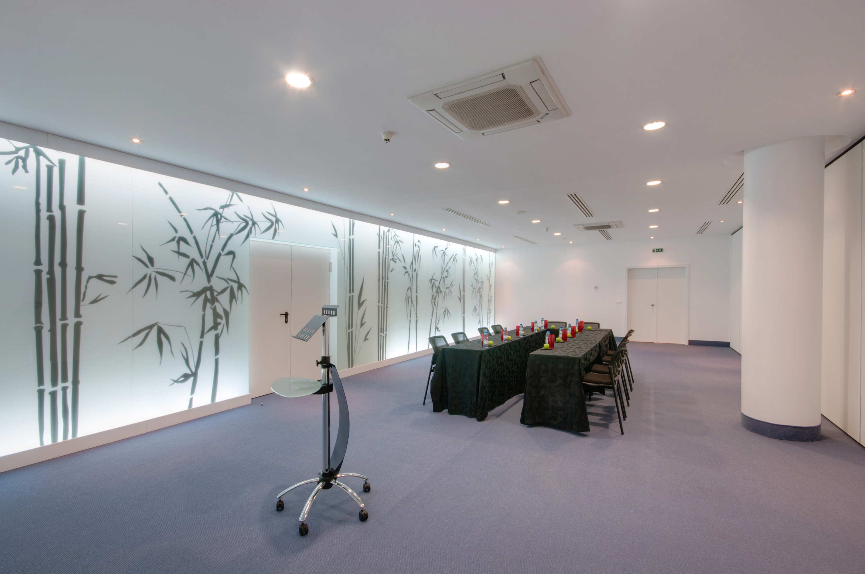 Modern conference room with black tables, lectern, and illuminated bamboo wall.
