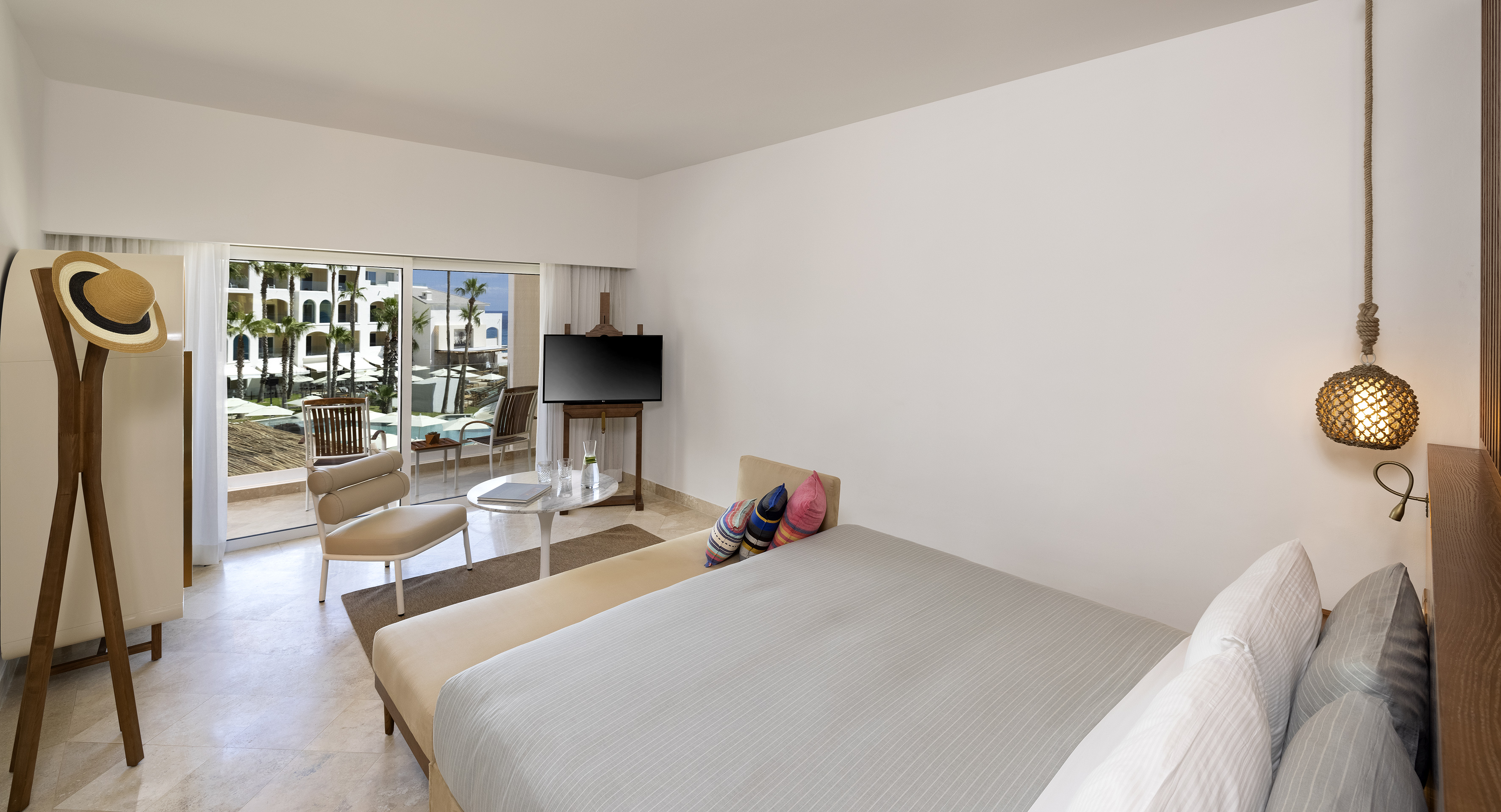 Modern hotel bedroom with patio, pool view, and palm trees.