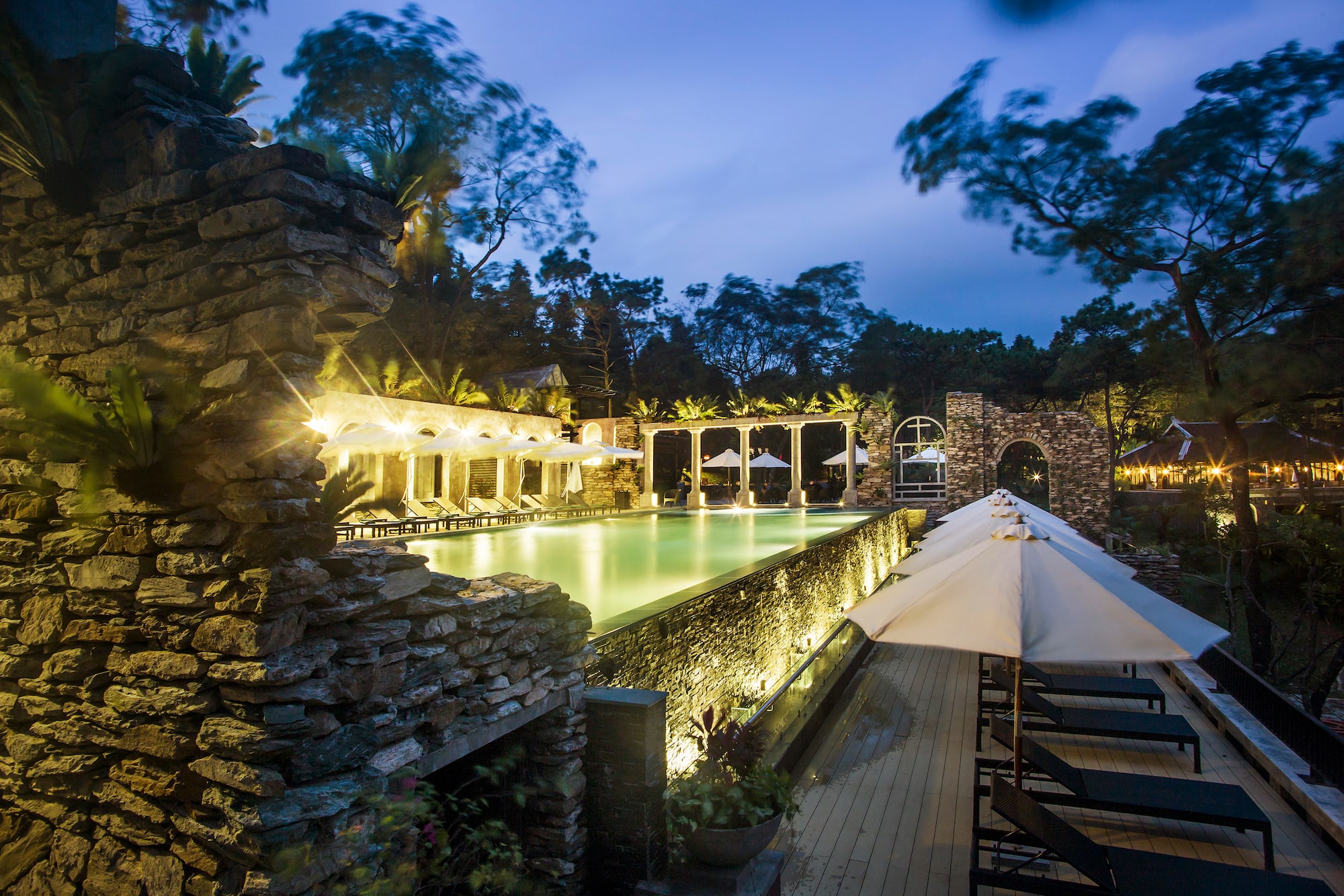 a pool with umbrellas and chairs in front of a stone building