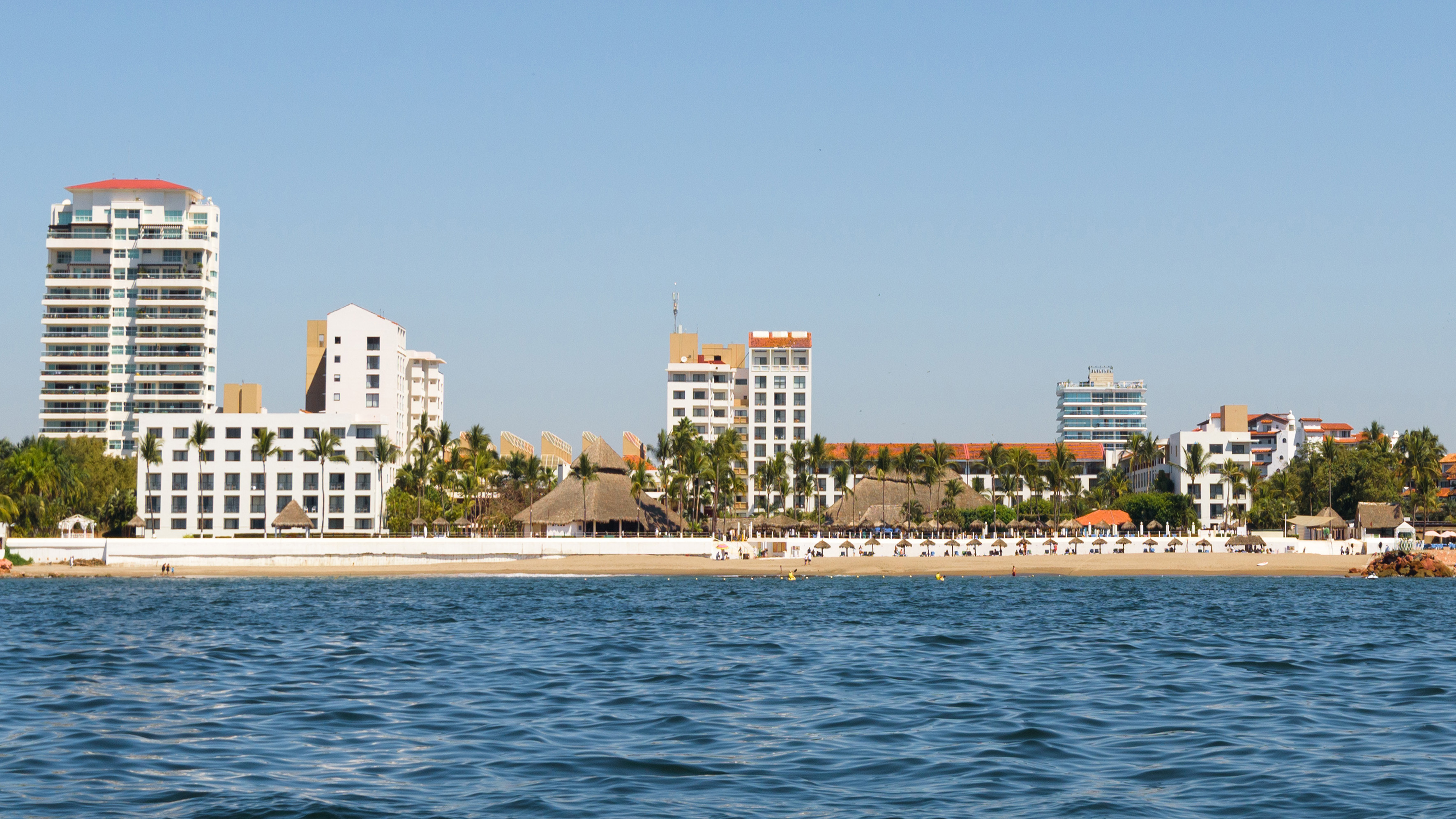Beachfront hotels and palm trees along a sandy coast with blue ocean.