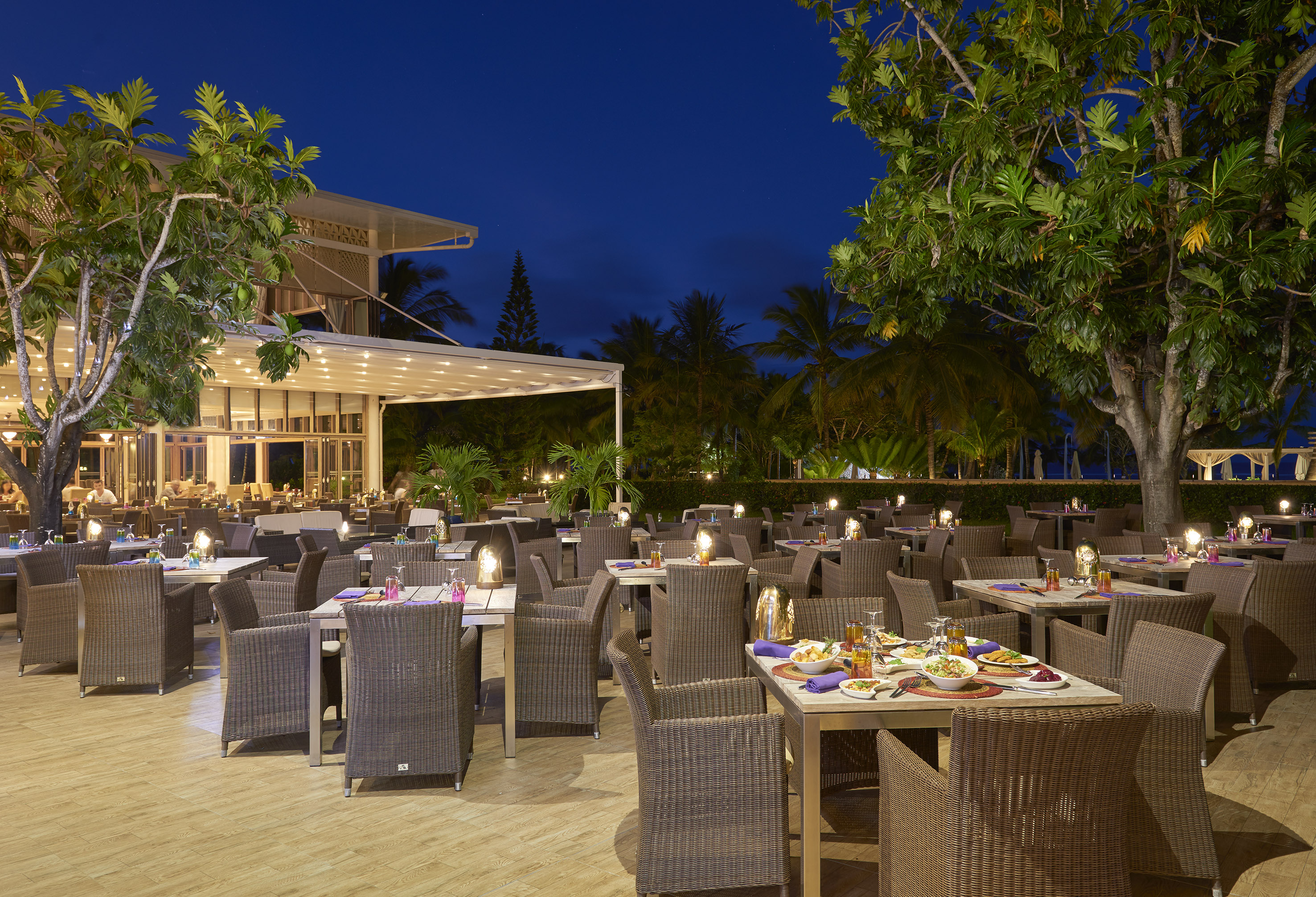 Tropical resort restaurant patio at night, tables set for outdoor dining.